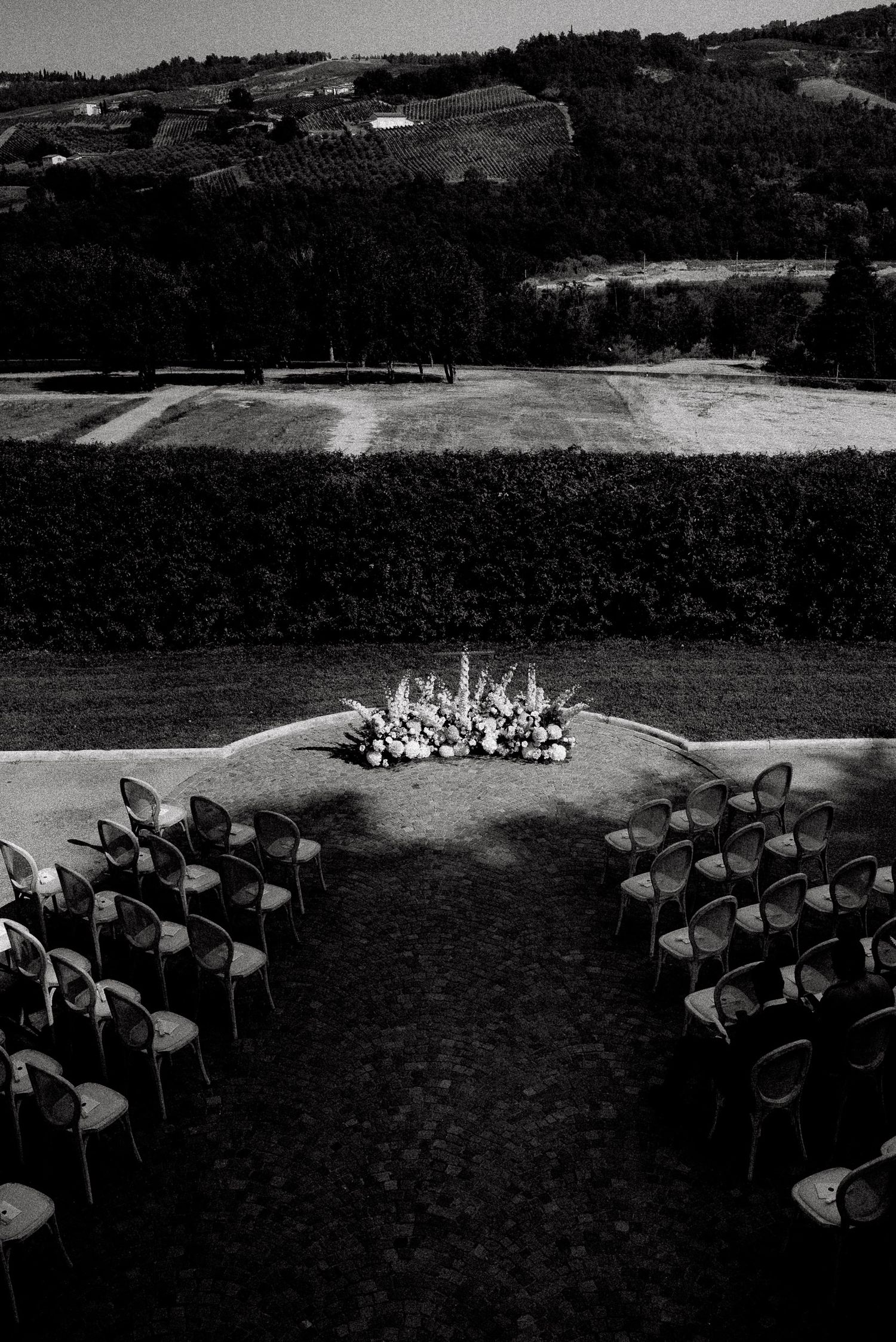 Black and white outdoor wedding ceremony setup with chairs, floral arrangement, and scenic rolling hills backdrop.