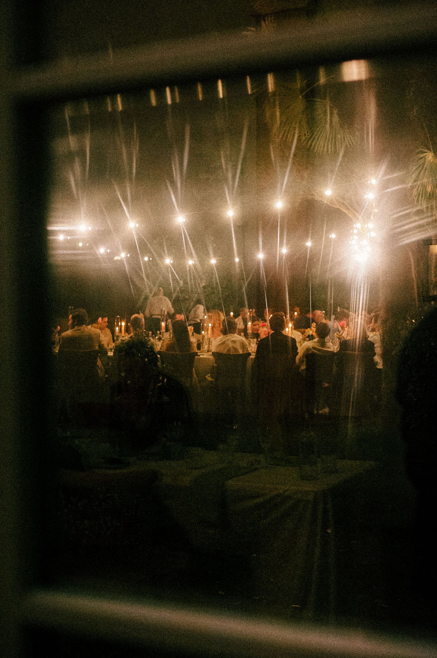 Elegant outdoor evening reception with warm string lights glowing above guests seated at decorated tables.