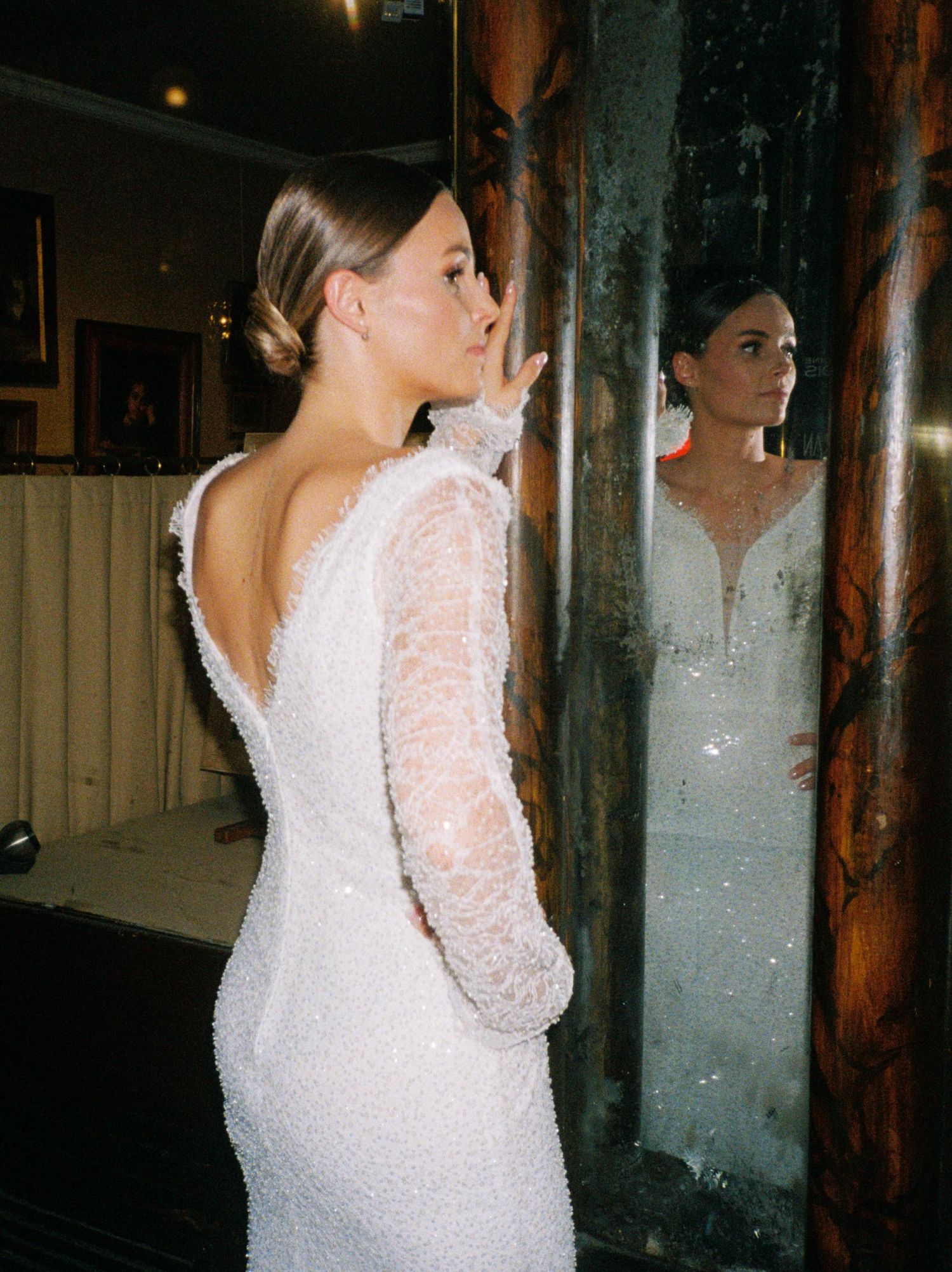 A bride in a white lace long-sleeved wedding dress poses in different angles showing the elegant open back design.