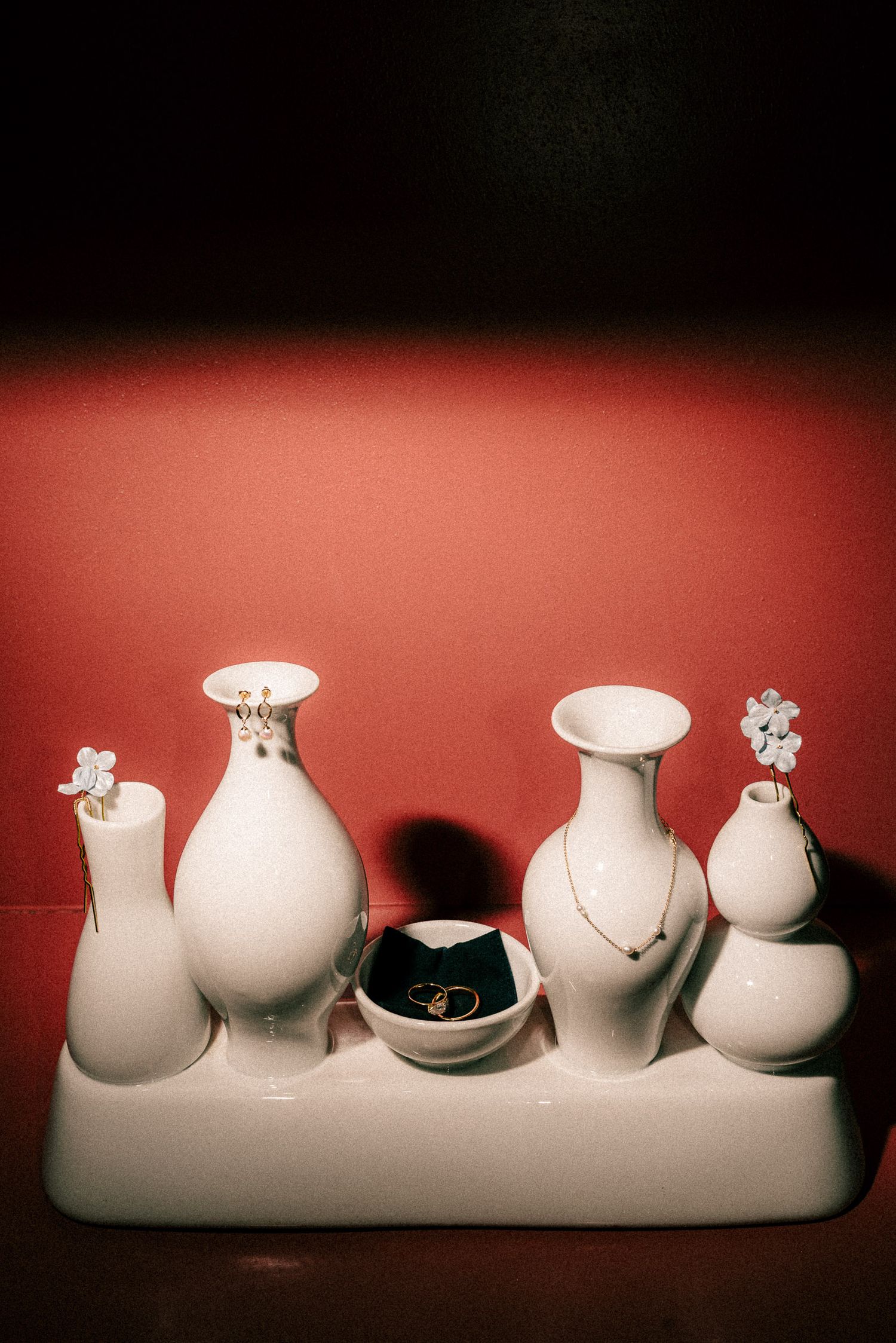 White ceramic vase set displaying jewelry including rings, necklaces, and earrings against a red background.