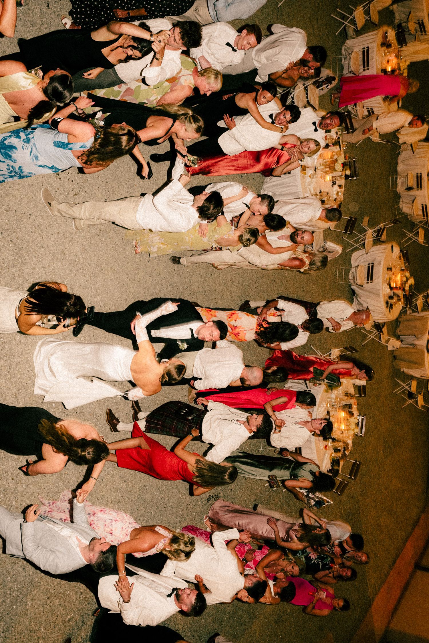 Aerial view of elegantly dressed wedding guests dancing and socializing at an outdoor evening reception.