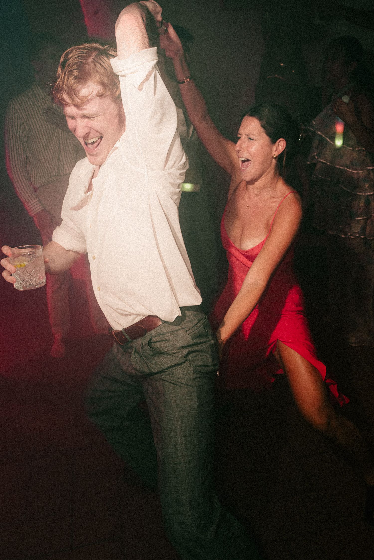 A man in white shirt and woman in red dress dancing energetically at a nightclub party.