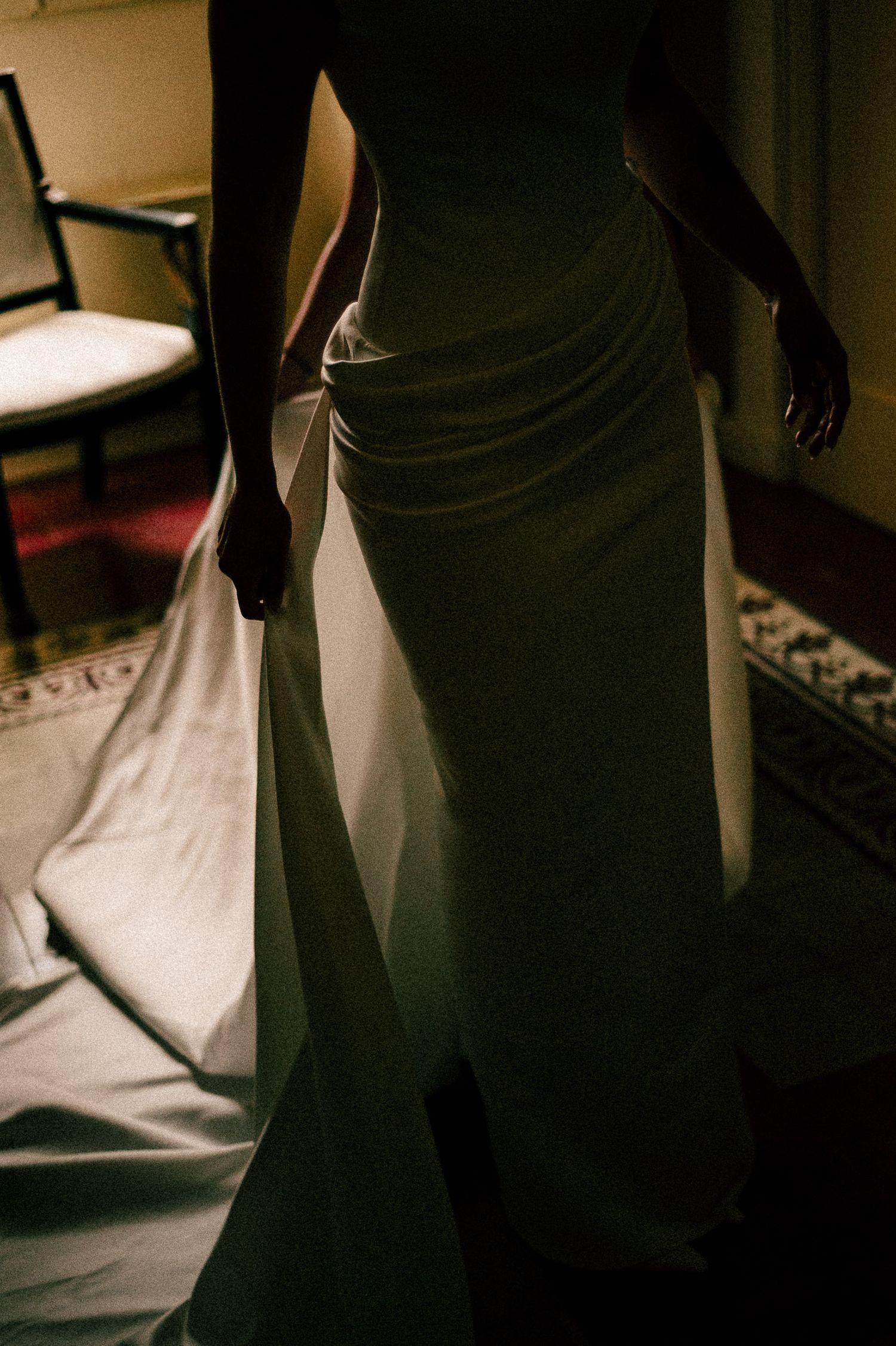 Silhouette of a bride in an elegant white wedding gown with a flowing train in a dimly lit room.