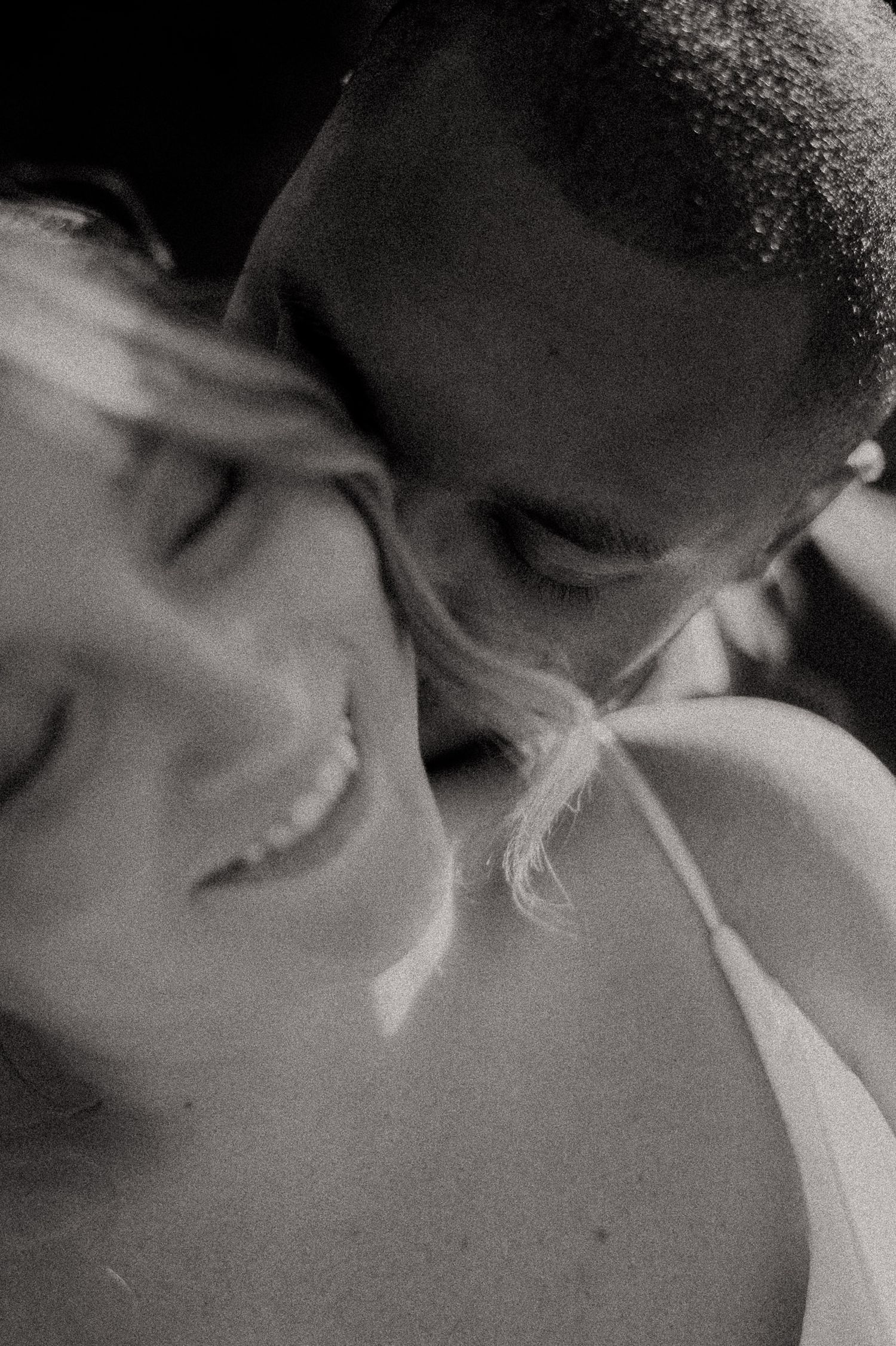 Black and white close-up of a couple sharing an intimate moment, man nuzzling woman's neck as she smiles softly.