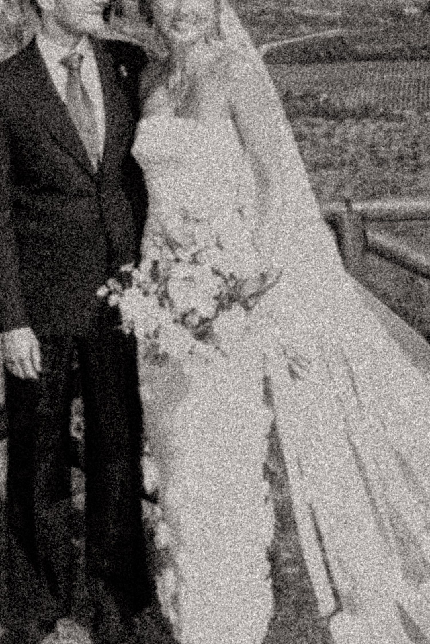 Black and white wedding photo of bride in white gown holding bouquet beside groom in dark suit.