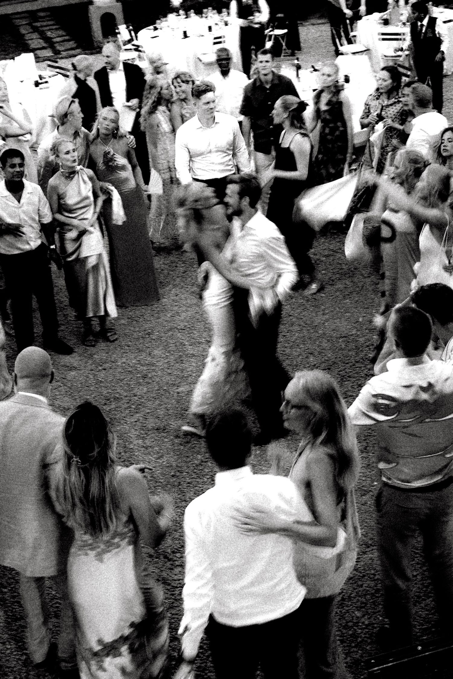 Black and white photo of elegantly dressed guests dancing and socializing at an indoor wedding reception.