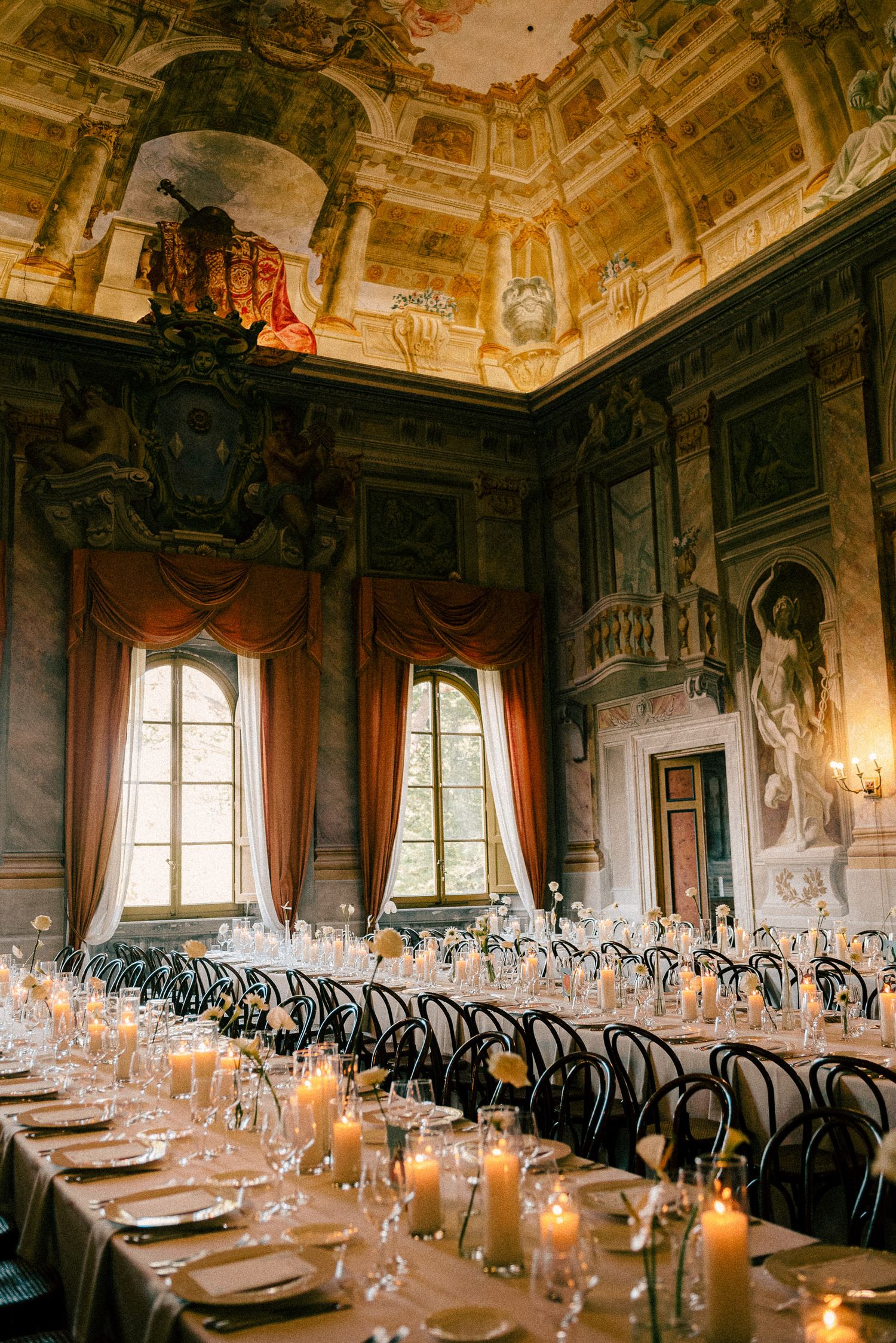 Elegant banquet hall with frescoed ceilings, candlelit tables, and draped windows for a formal dinner event.