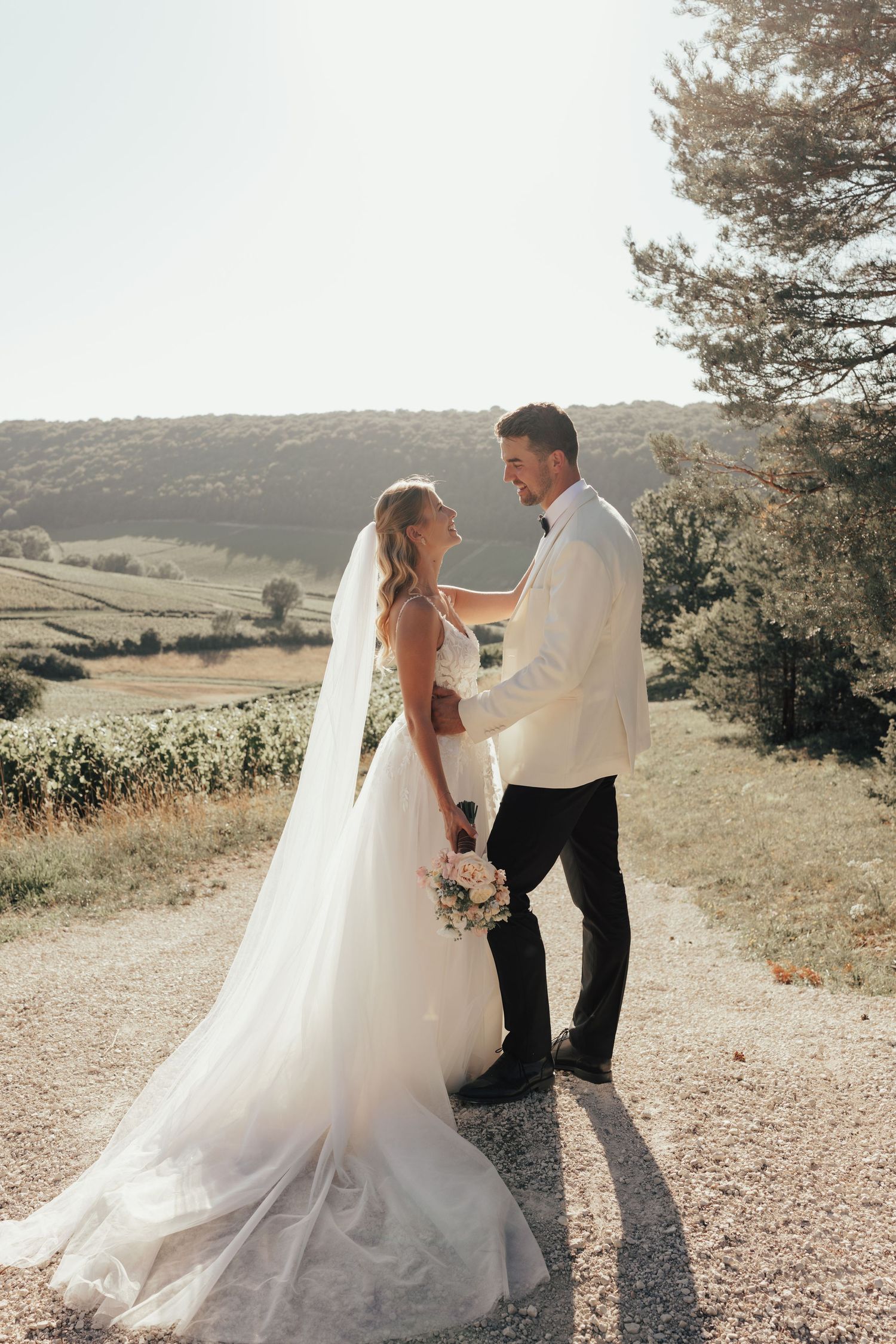 Bride and groom share romantic moments during golden hour photo session on a scenic hilltop path.