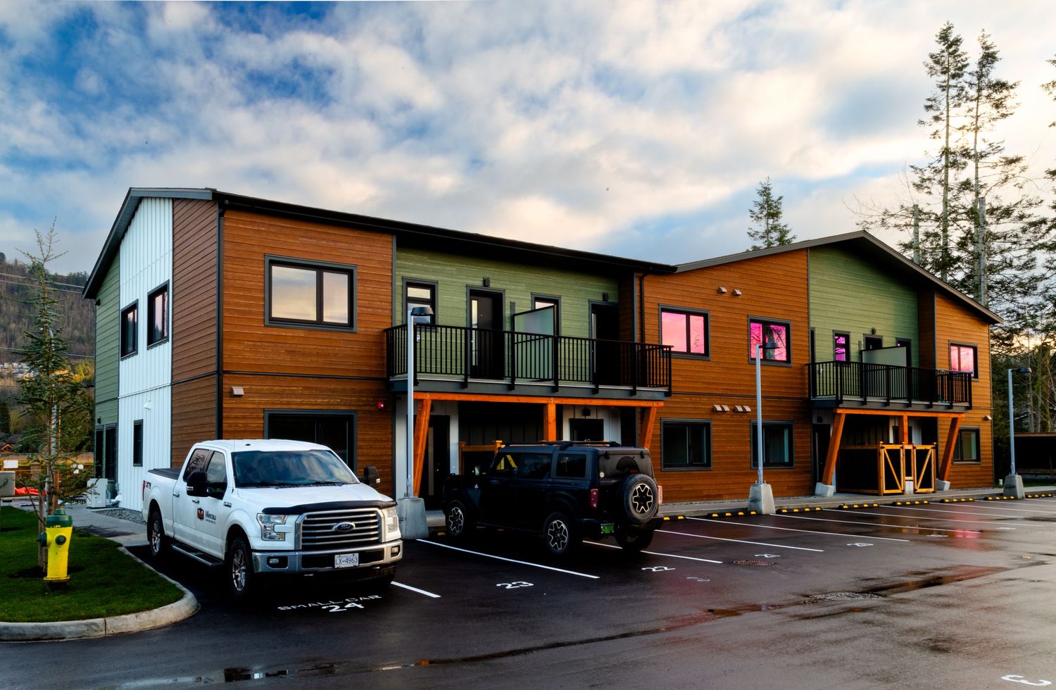 Colorful modern townhomes with wood accents and parking spaces under cloudy skies.