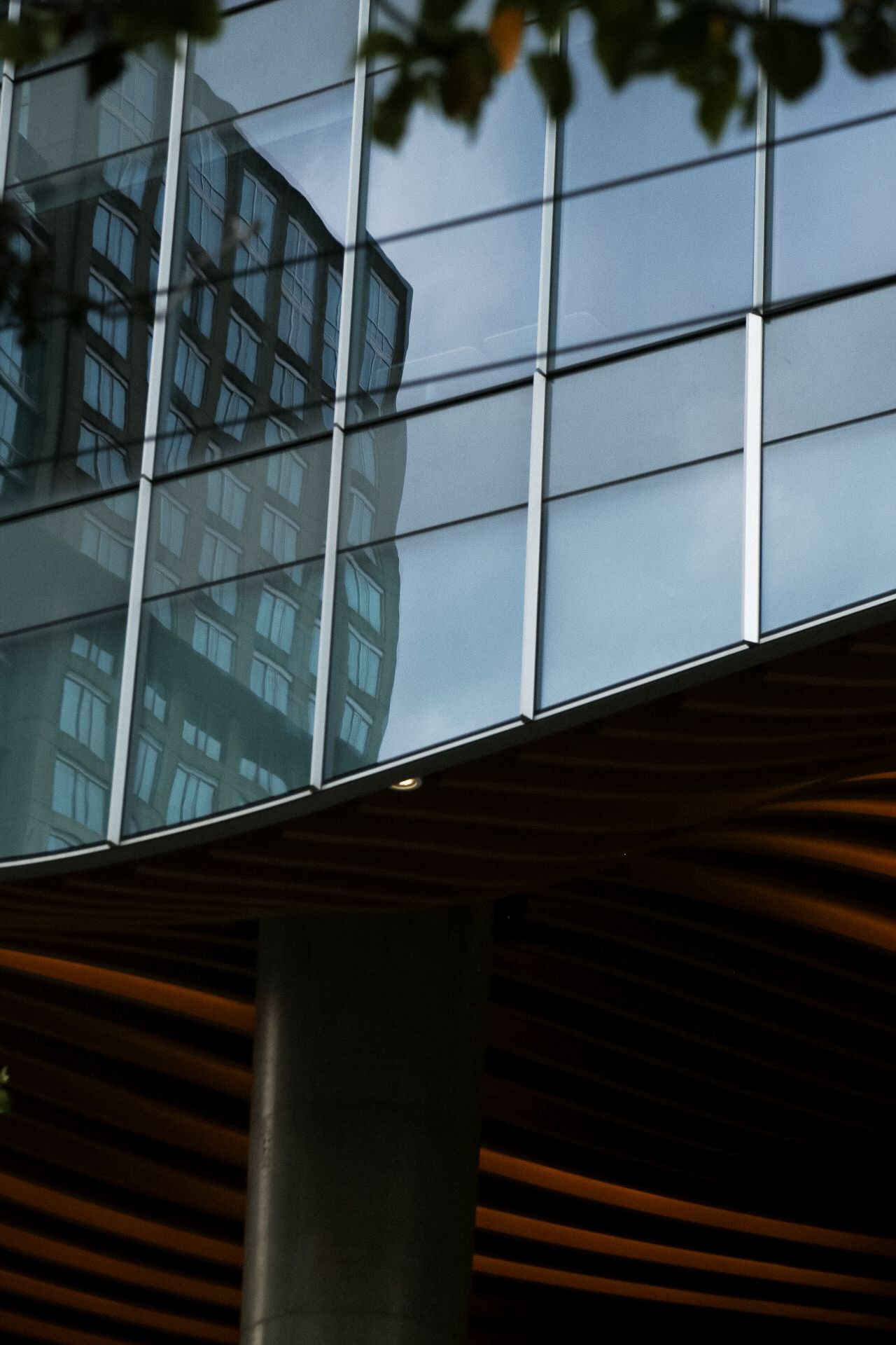 Modern glass building facade with reflective windows and architectural details against a cloudy sky.