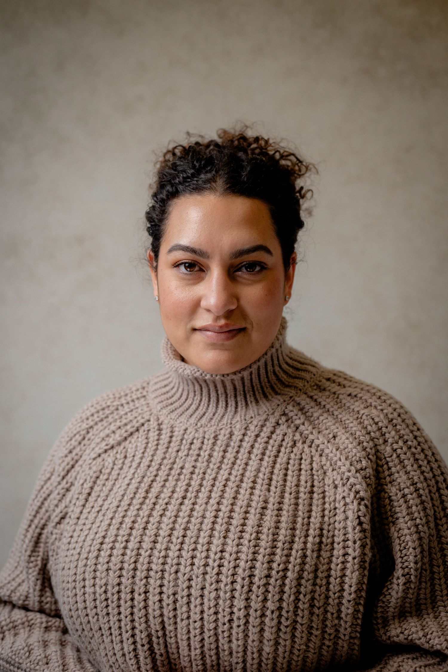 Portrait of person wearing a chunky knit turtleneck sweater against a neutral background.
