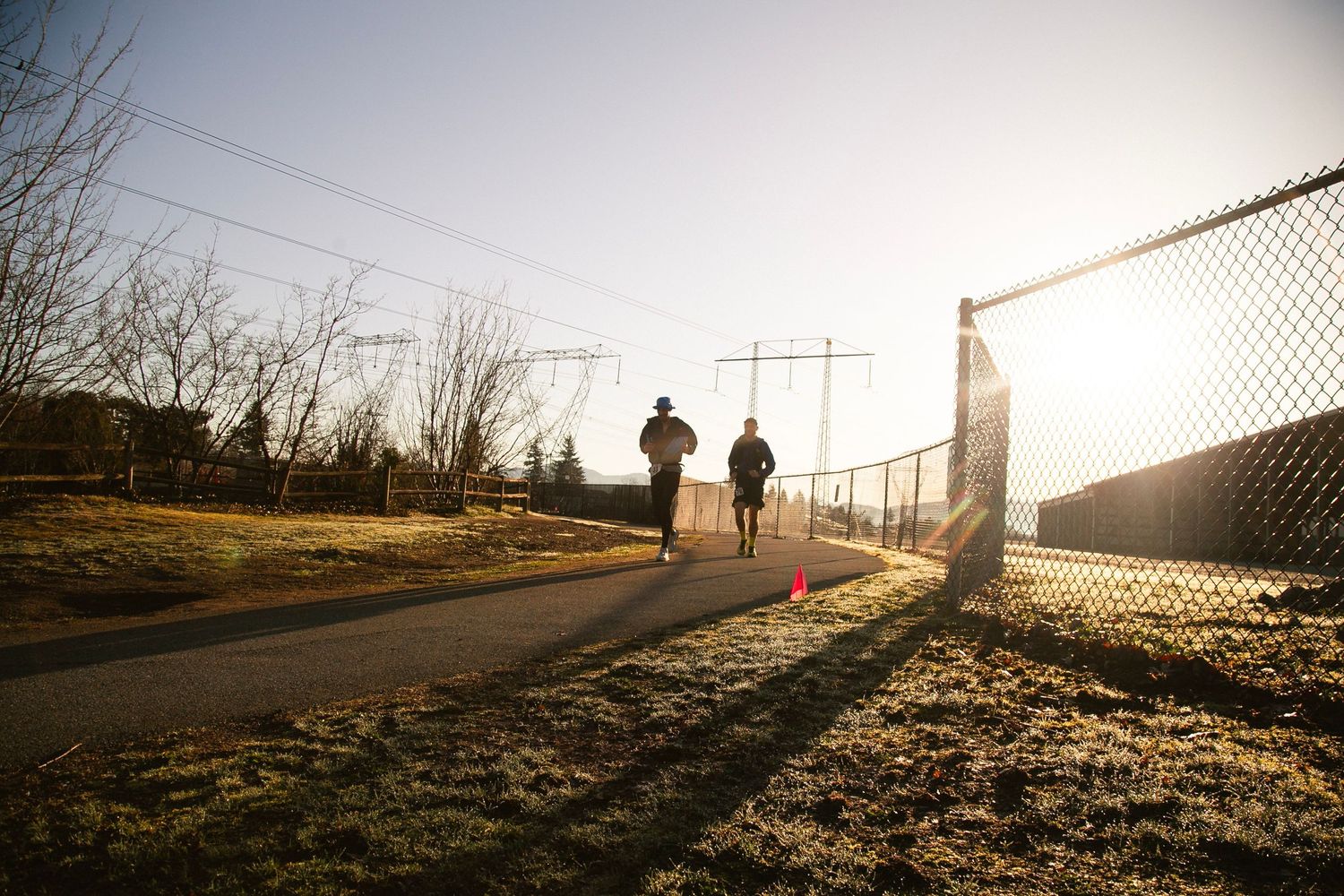 Two joggers running on path during golden hour with long shadows and fence.