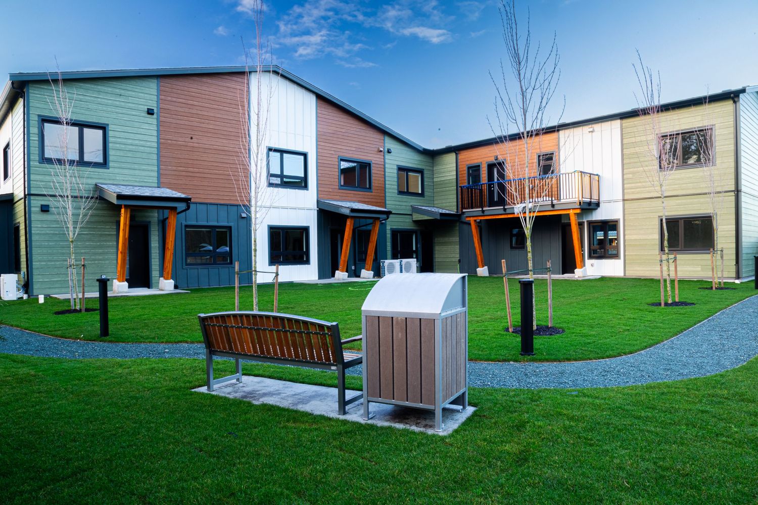 Modern colorful townhouses with balconies surrounding a landscaped courtyard with benches.