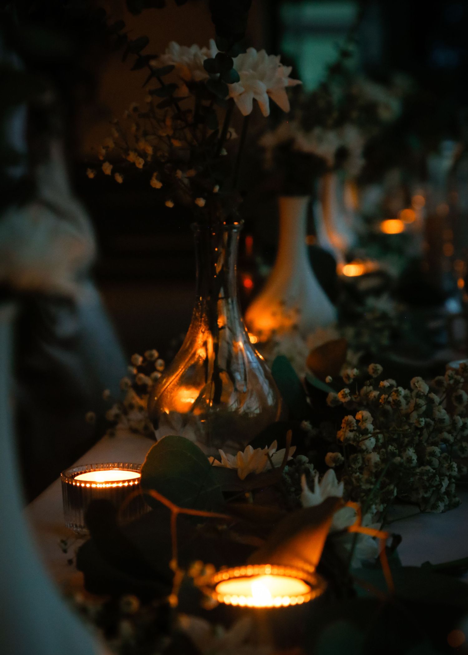 Romantic candlelit table setting with ethereal flowers in glass vases creating ambient lighting.