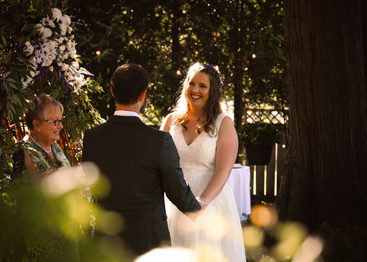 Outdoor wedding ceremony under trees with twinkling lights at dusk.