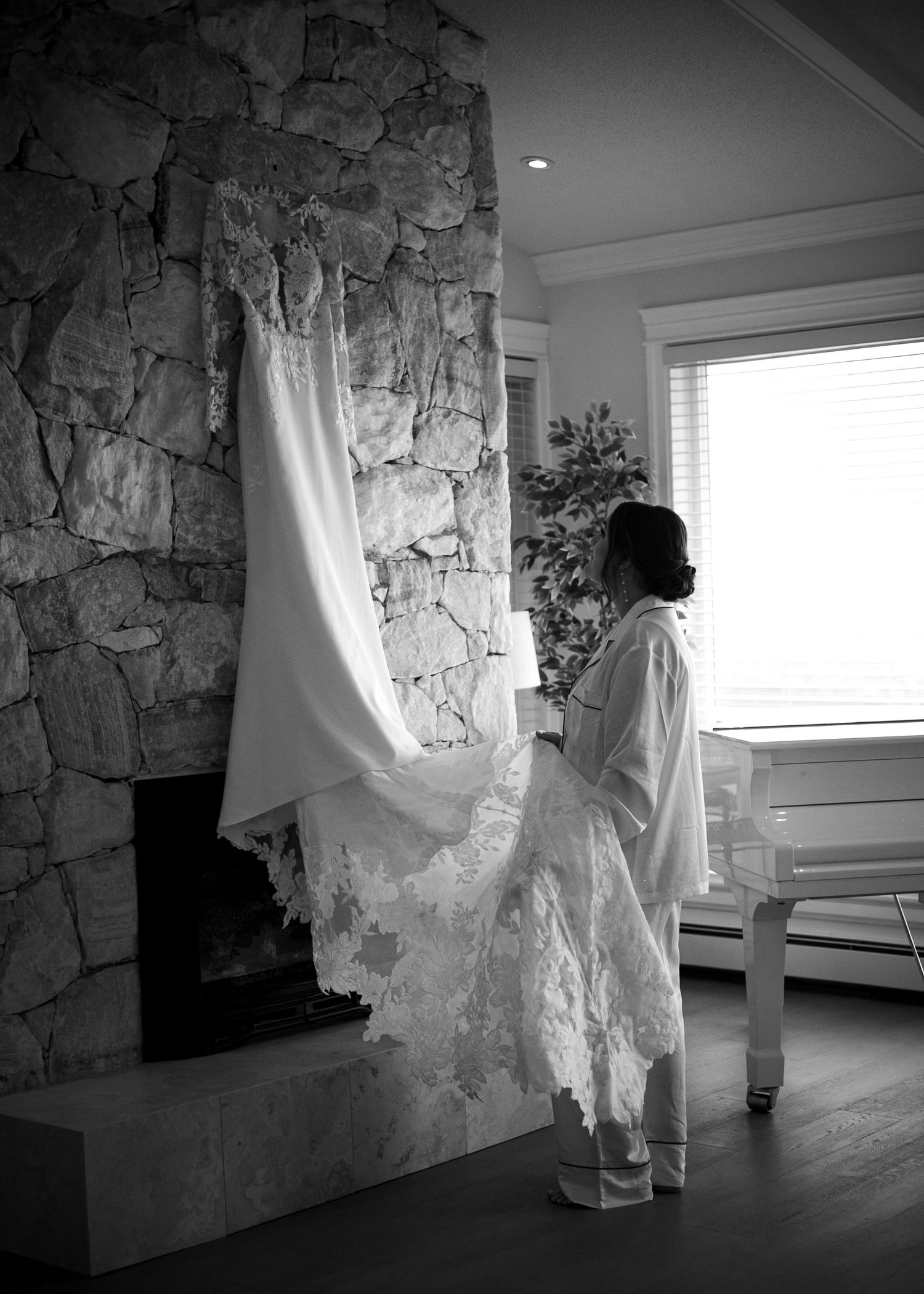 Black and white photo of wedding dress hanging on stone wall near window.