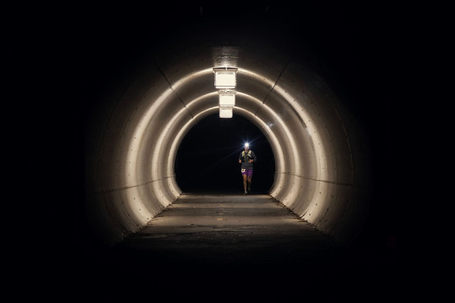 Illuminated curved tunnel with glowing archways leading to dark exit.
