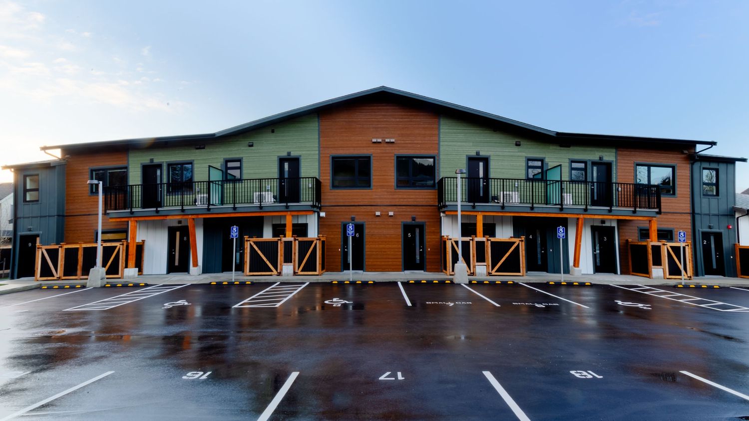Modern two-story commercial building with wood accents and empty parking lot on a rainy day.