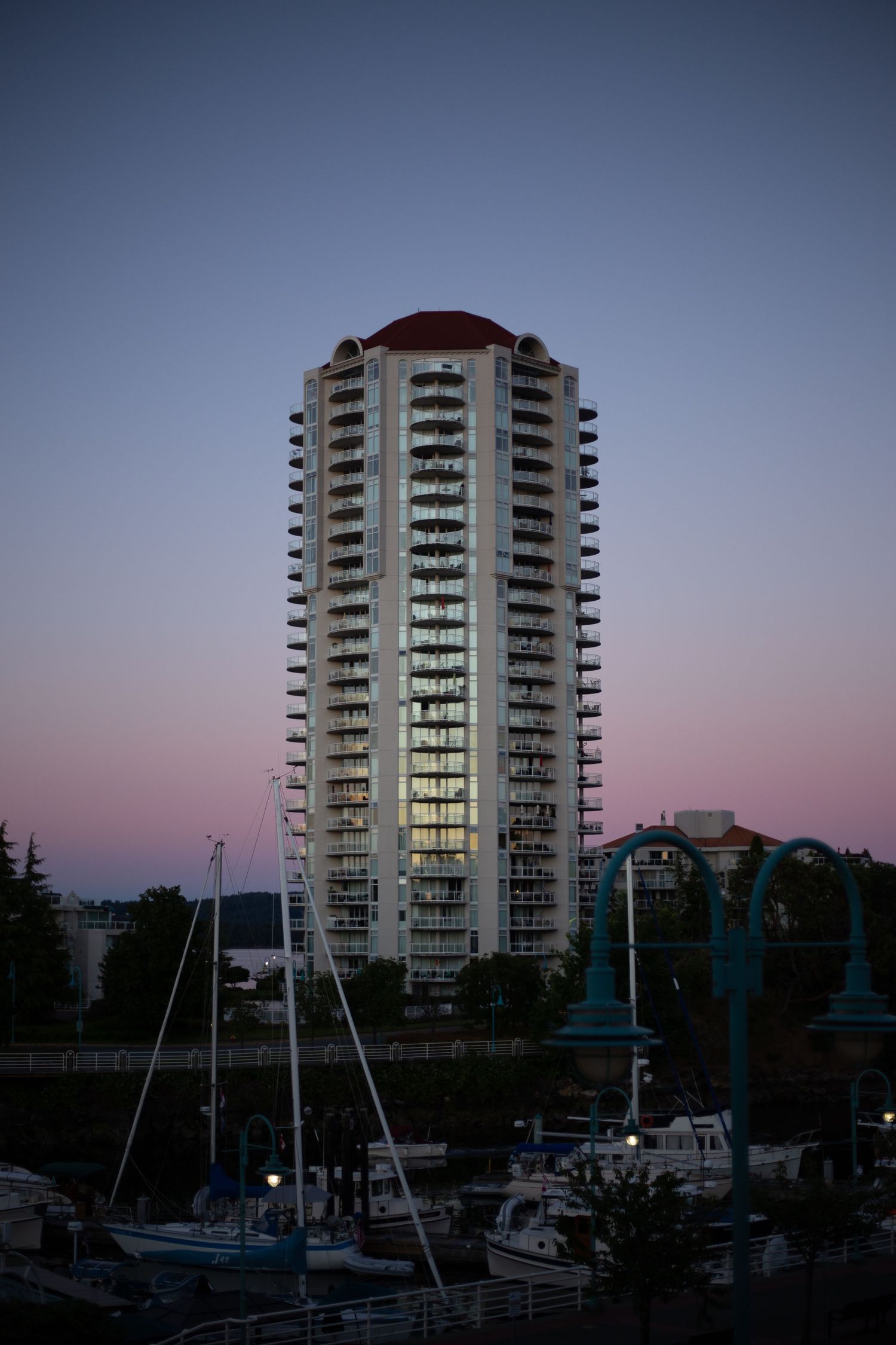 High-rise residential tower with balconies lit at dusk overlooking a marina.