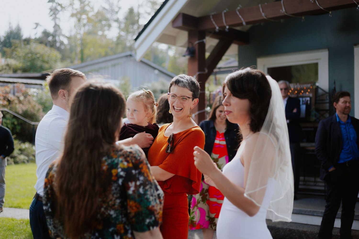 Wedding guests gather outside on a sunny day, celebrating with the bride in her white veil.