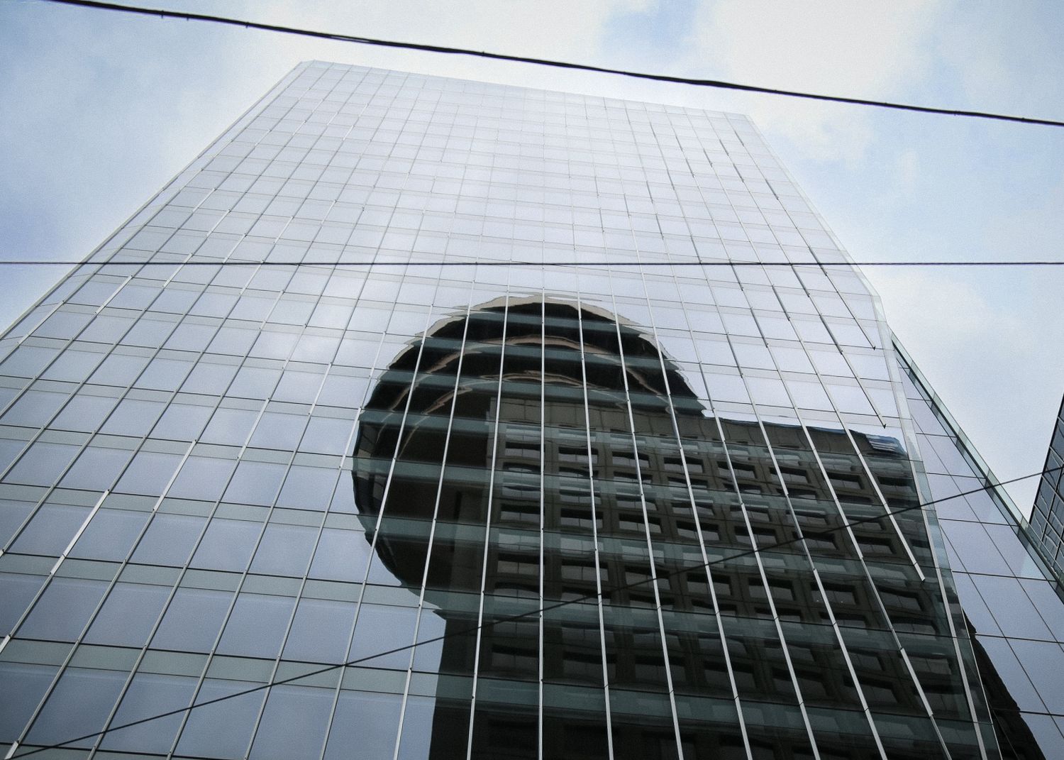Glass skyscraper photographed from below with power lines crossing the frame.