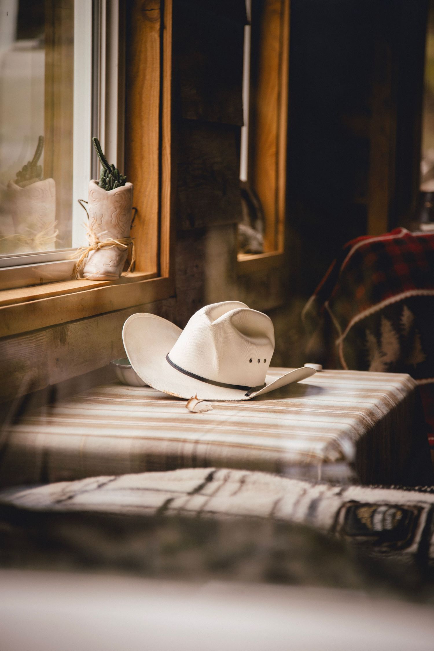 A white cowboy hat rests on a striped surface near a sunlit window.
