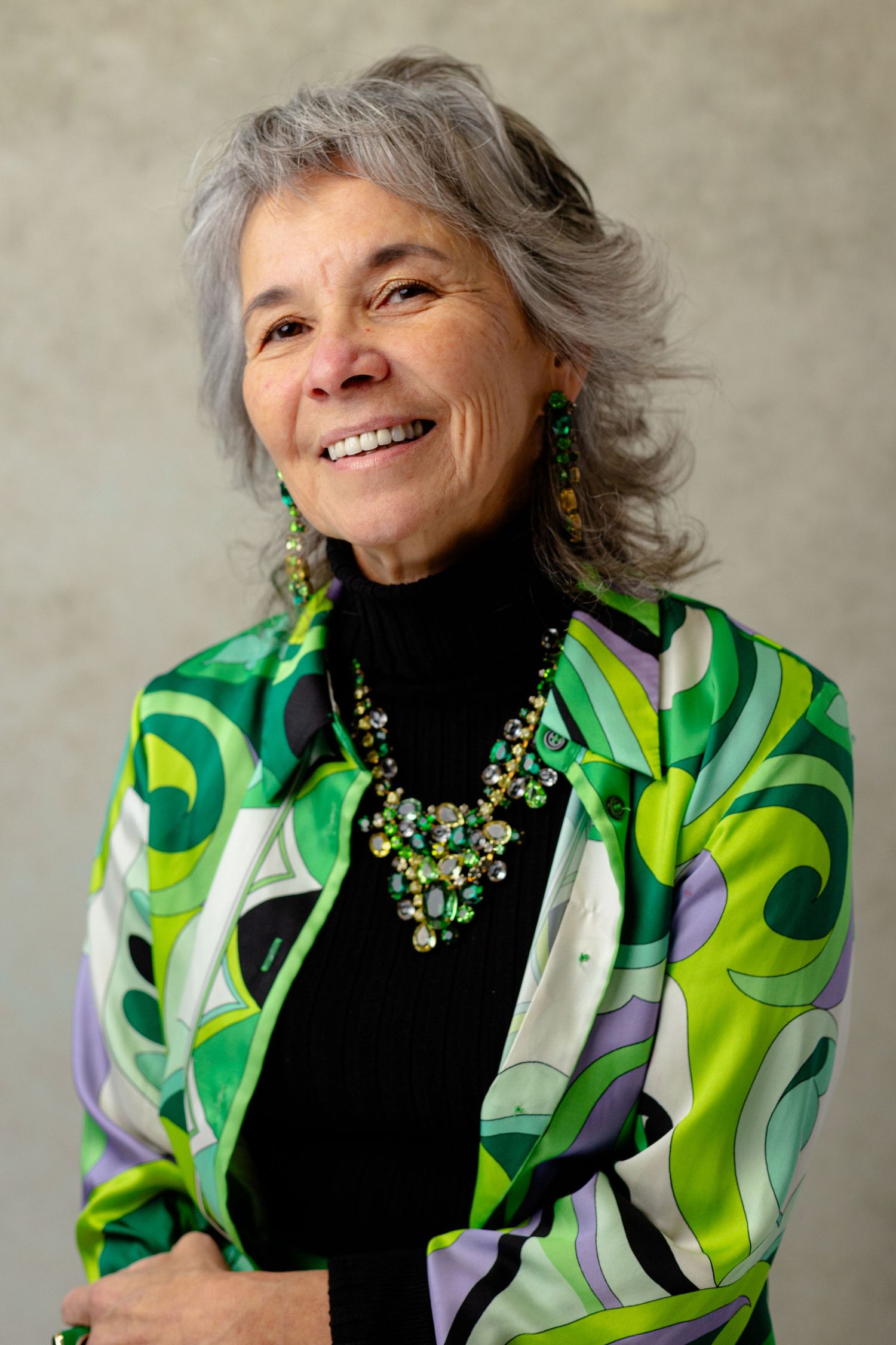 A portrait showing someone wearing a vibrant green patterned jacket with statement jewelry.