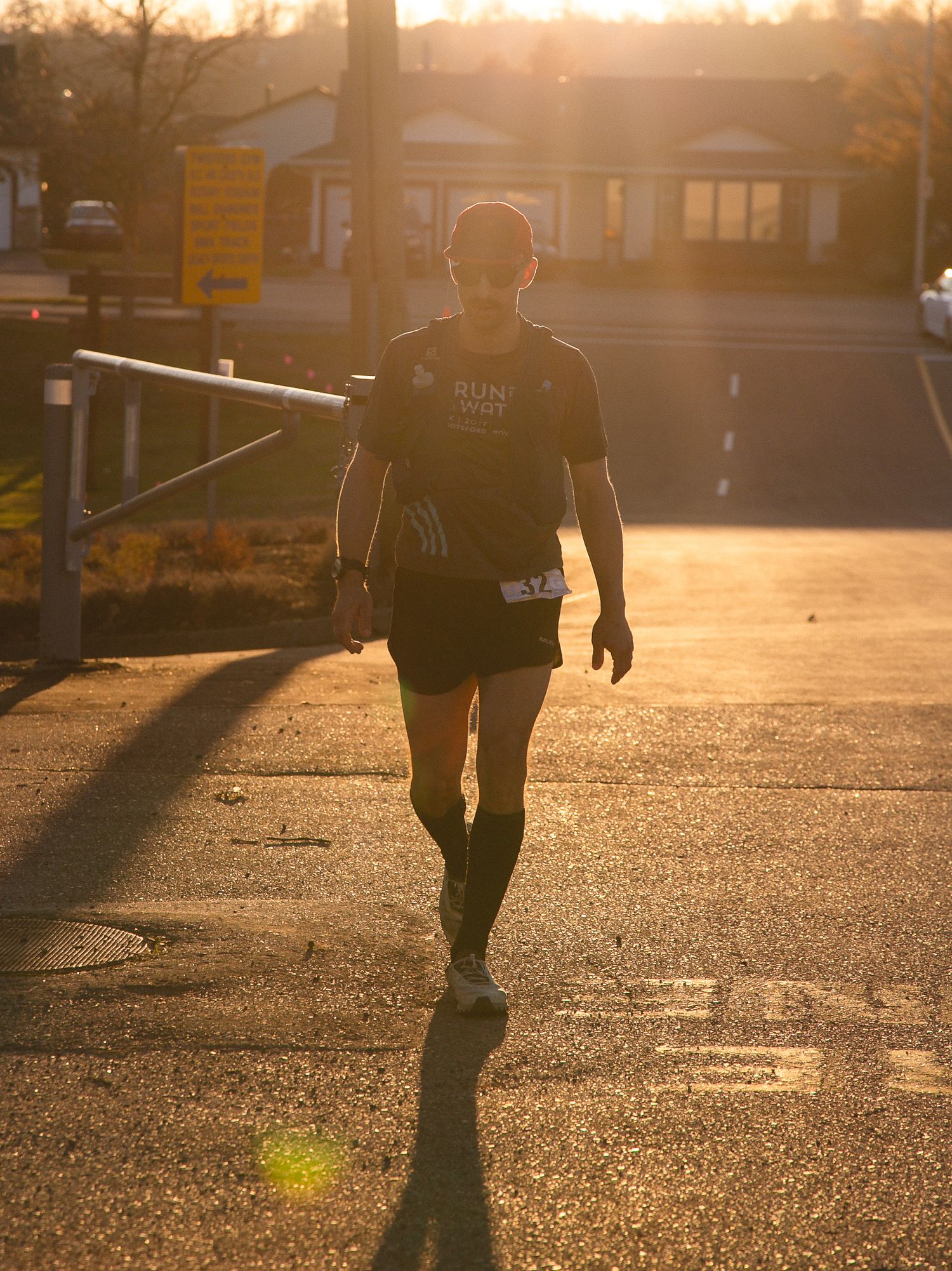Silhouette of a runner walking at sunset against a golden sky and buildings.