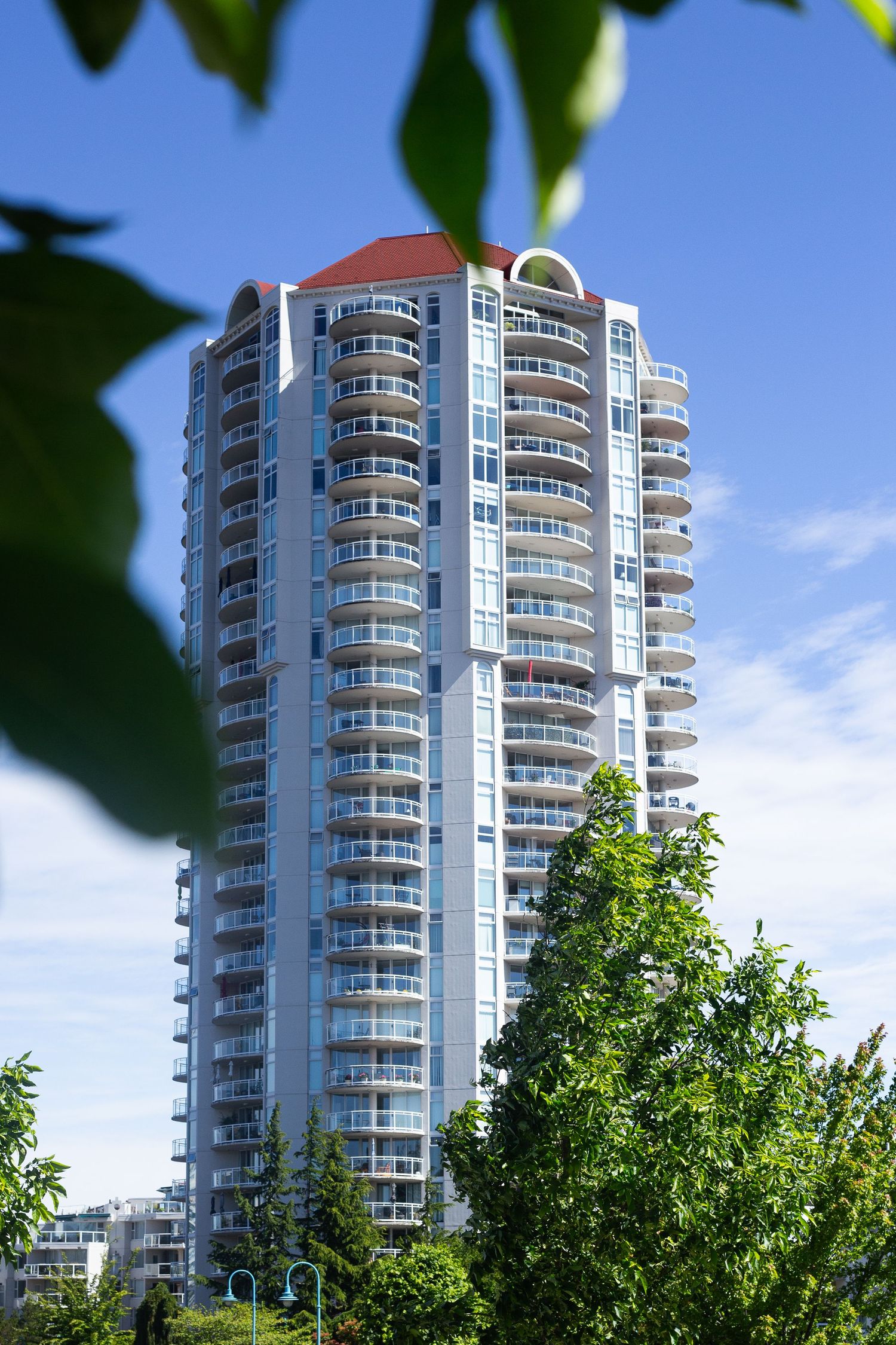 Luxury residential high-rise tower with curved balconies framed by green trees.