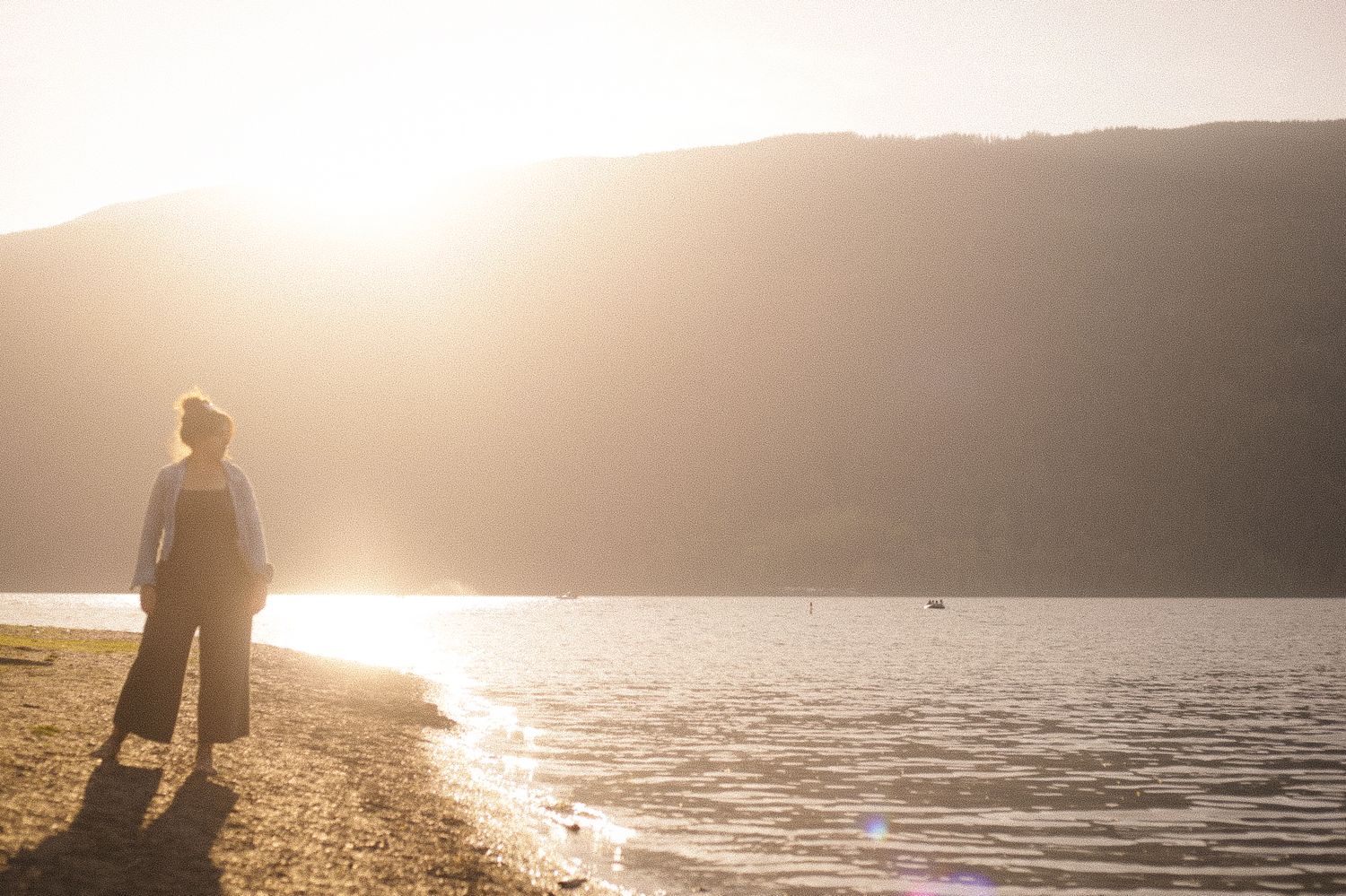 Silhouette standing by lakeside during golden hour sunset.