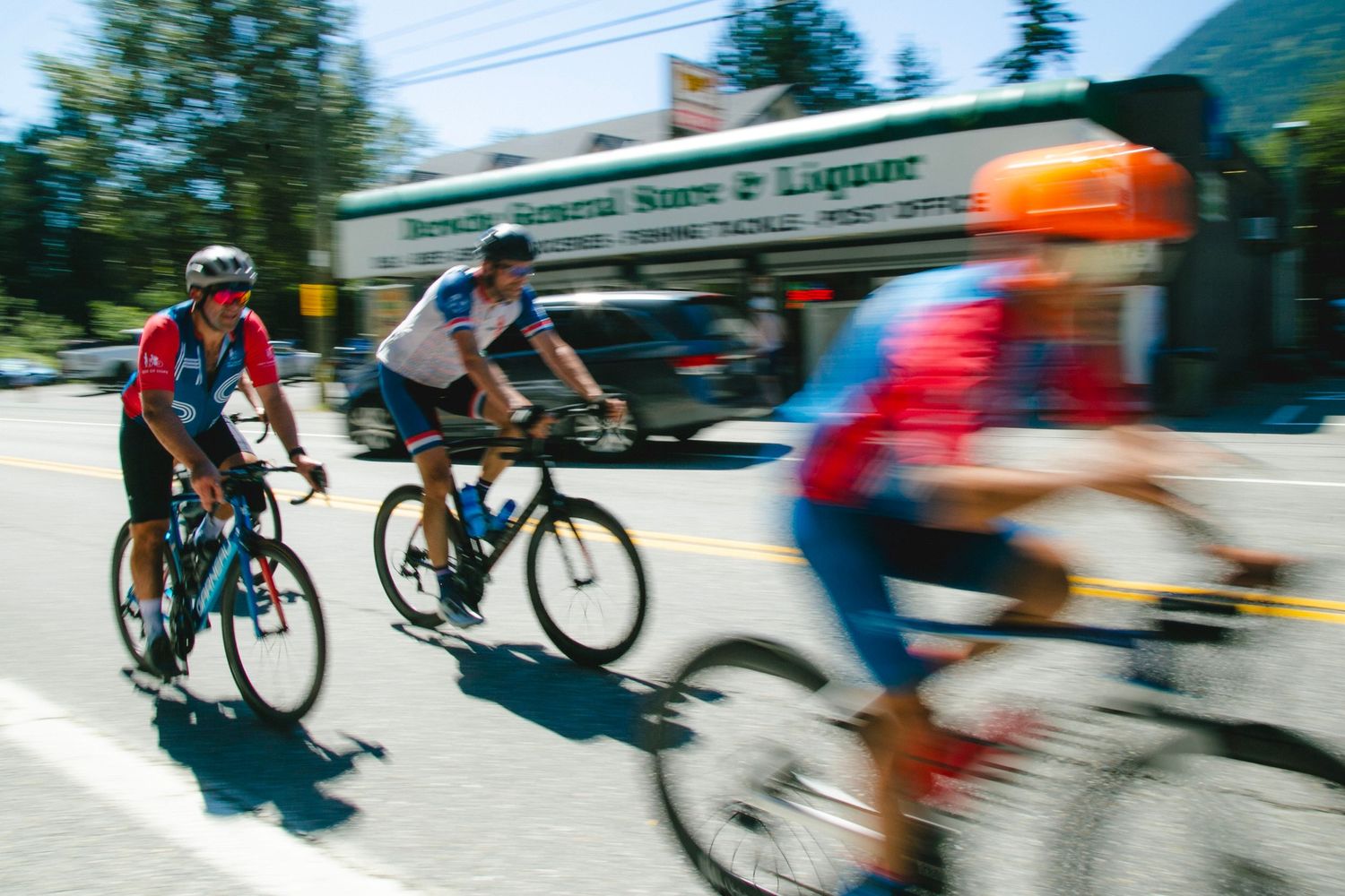 Motion blur of cyclists racing past building on sunny day.
