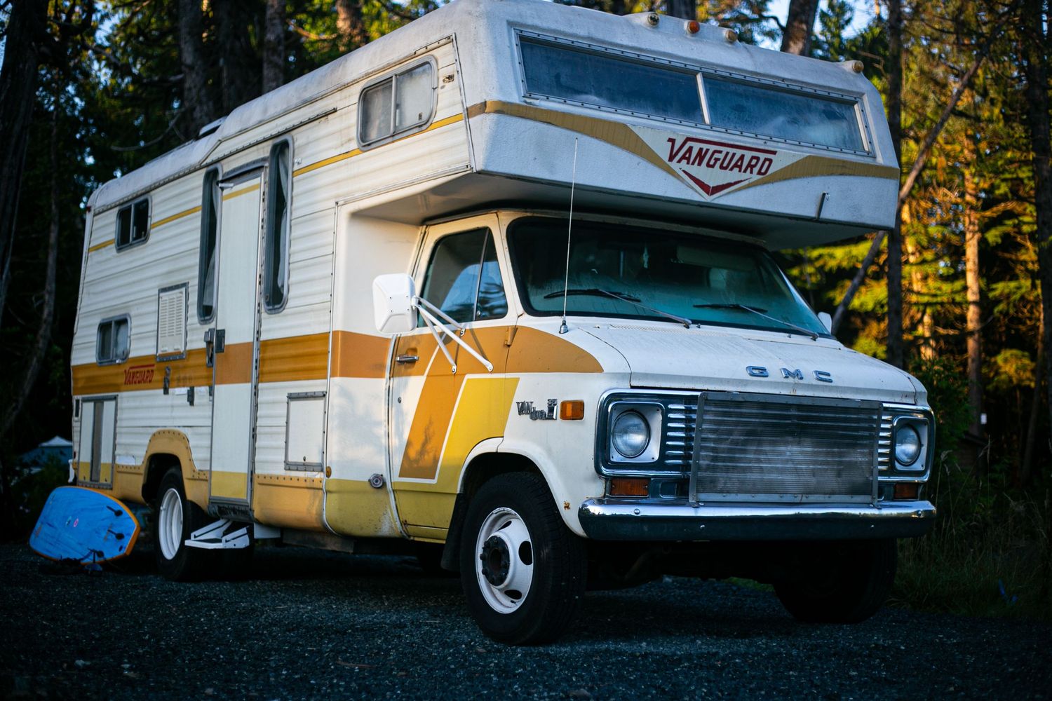 A vintage white and orange RV camper parked in a forested campground.