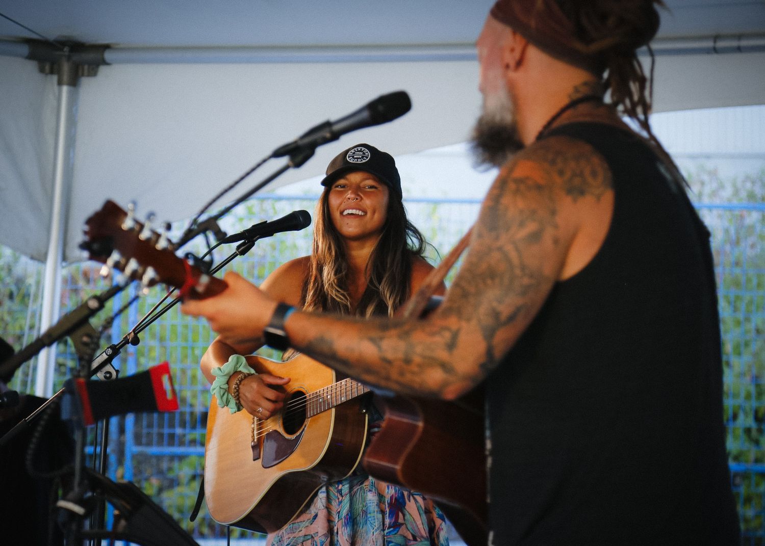 Musicians performing with acoustic guitars under a white tent at an outdoor festival.