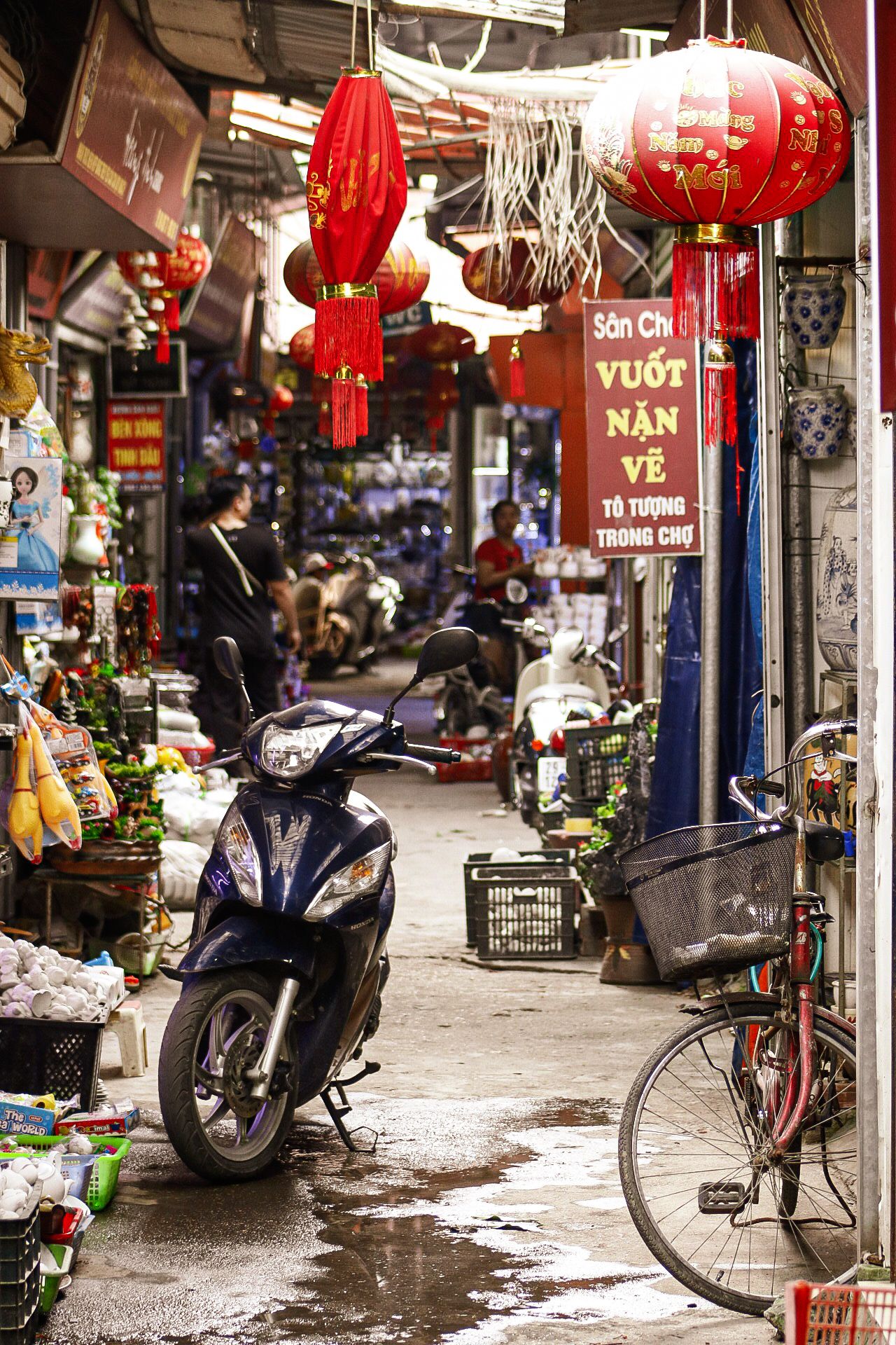 Vietnamese street market alley with red lanterns and parked motorbikes.