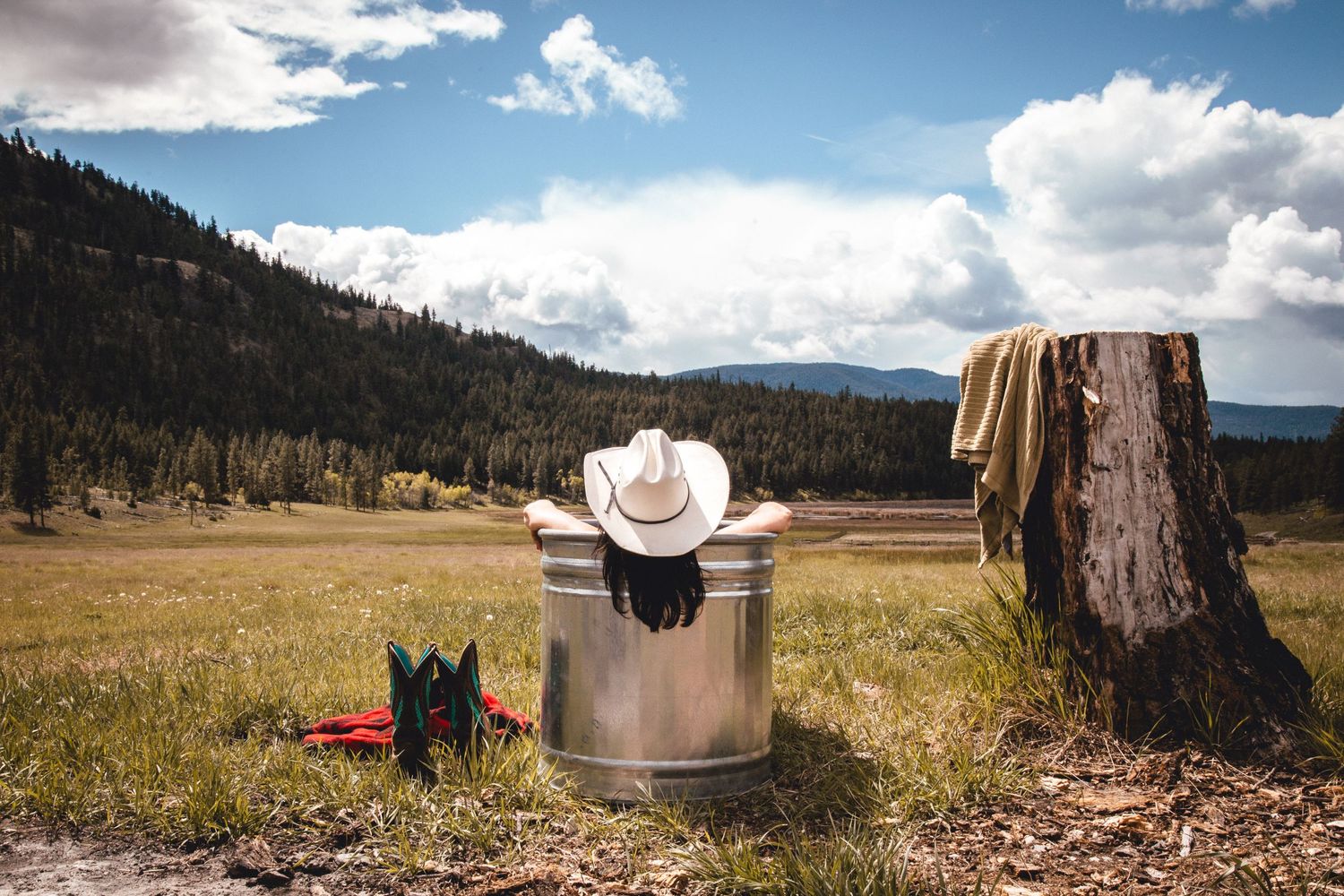 White cowboy hat on metal barrel against mountain landscape with tree stump.