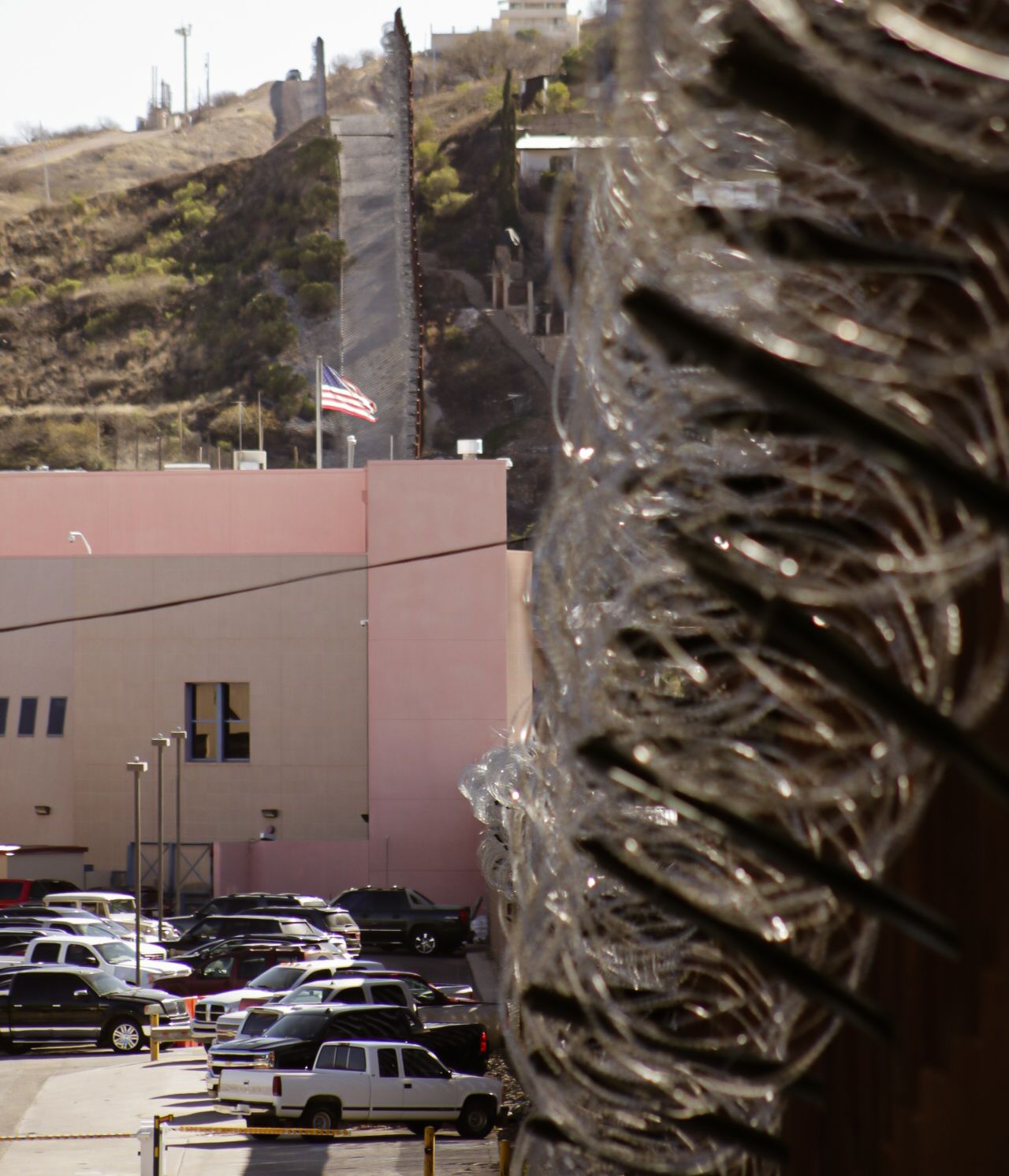 A pink industrial building with a parking lot full of vehicles against a hillside.