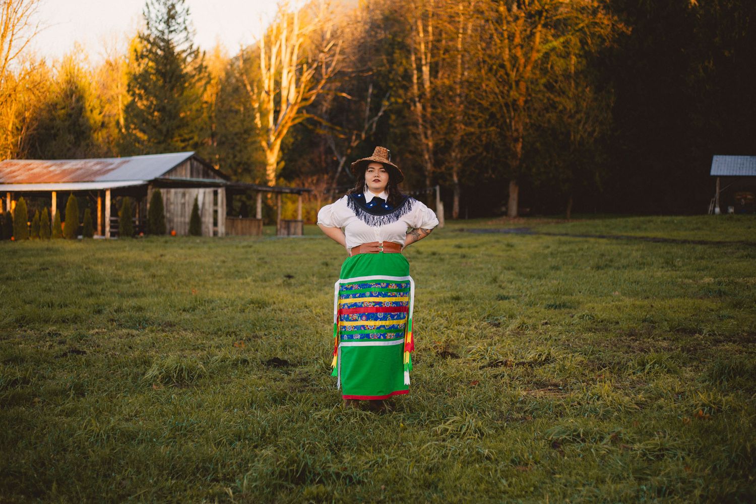 Person standing in a grassy field at sunset with a festive green Christmas-themed display.