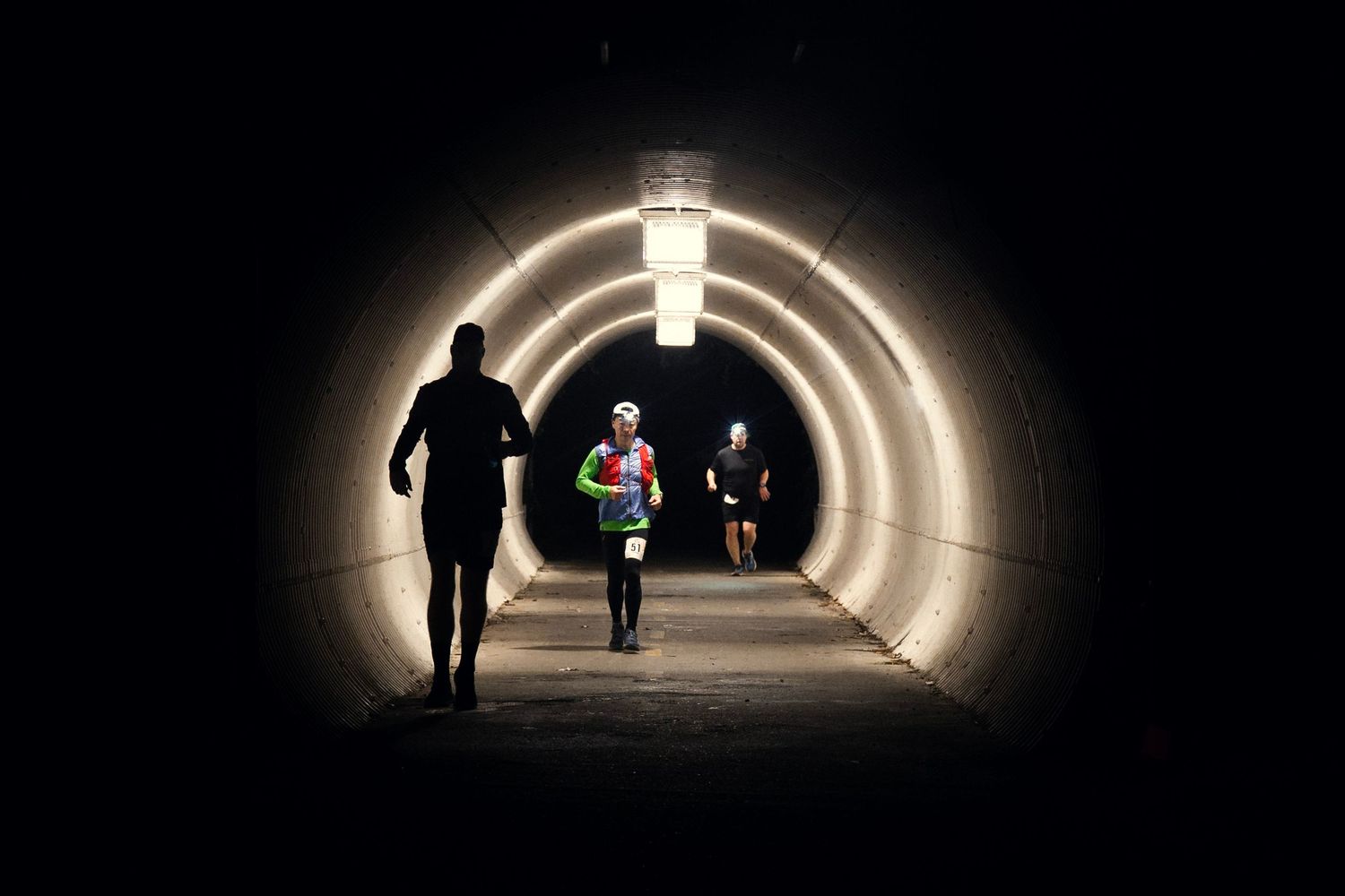 Silhouettes of runners in a brightly lit tunnel with circular architecture.
