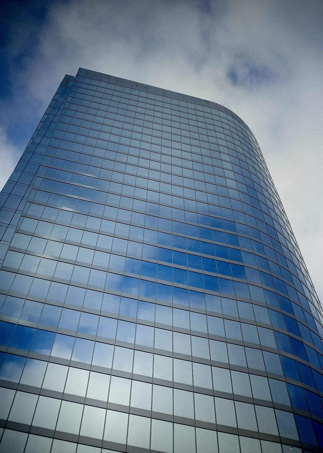Modern glass office building with curved facade reflecting clouds and sky.