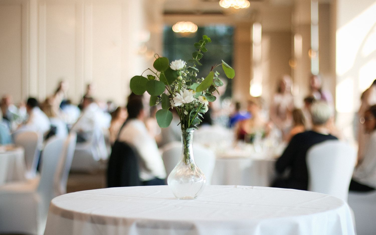 Elegant white floral centerpiece on round table at formal wedding reception venue.