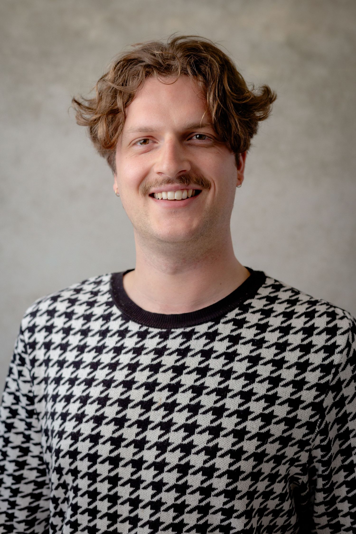 A portrait of someone in a black and white houndstooth sweater against a gray background.
