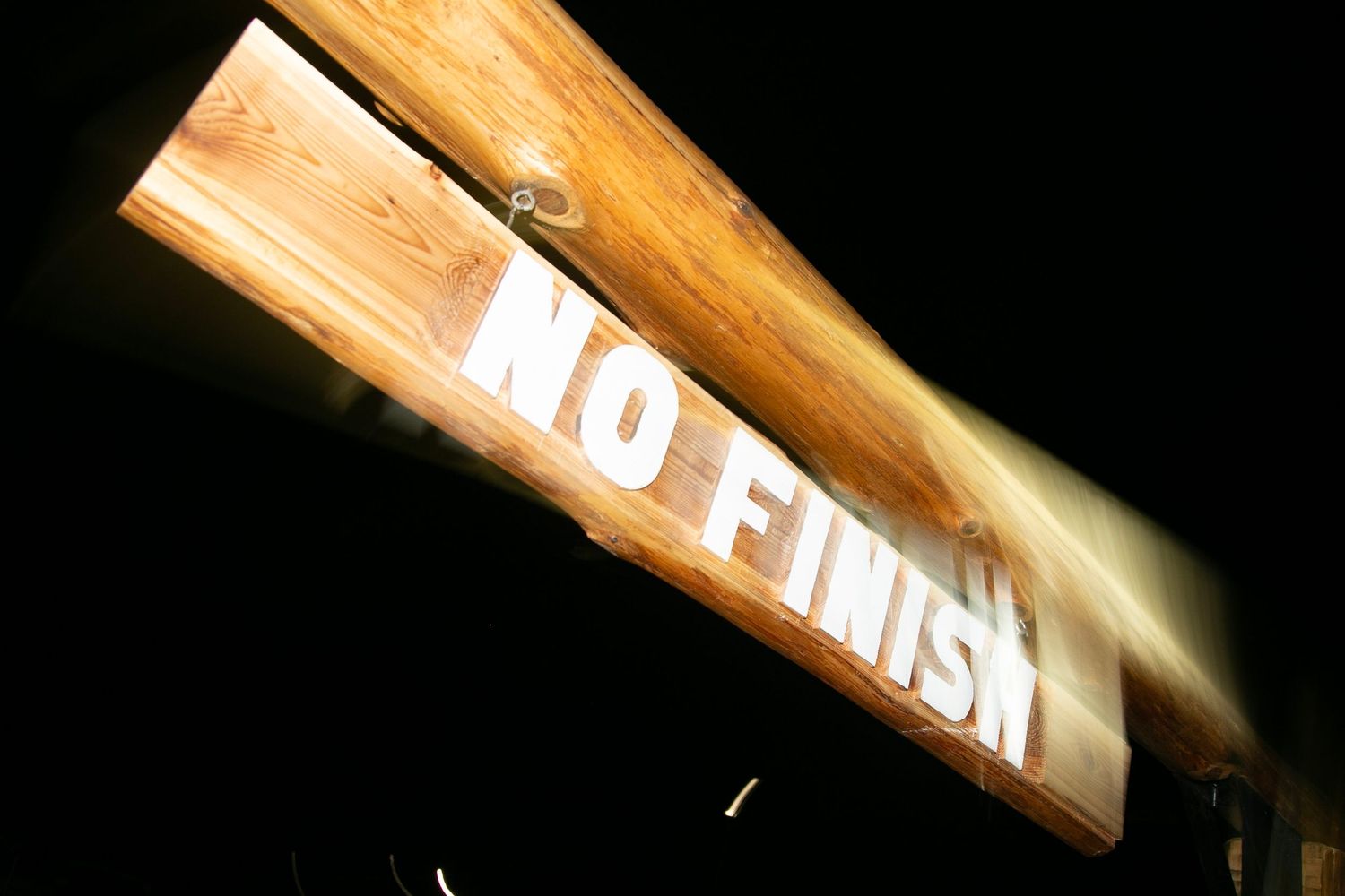 Illuminated wooden sign reading 'TO FINISH' photographed at night.