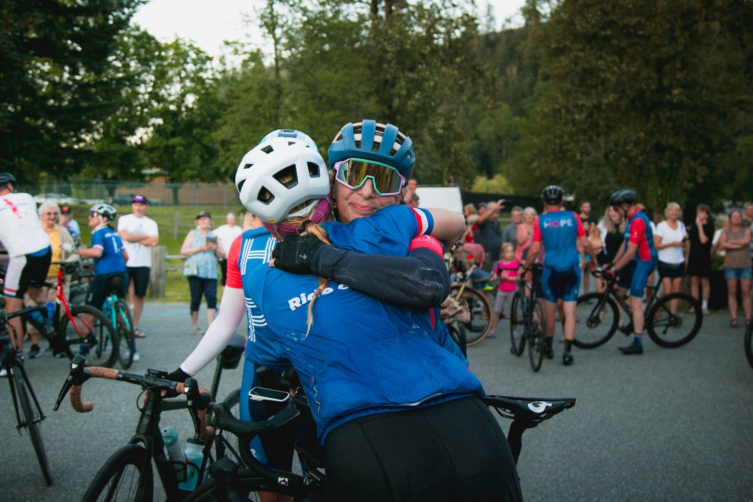 Cyclists in bright jerseys embrace during outdoor cycling event.