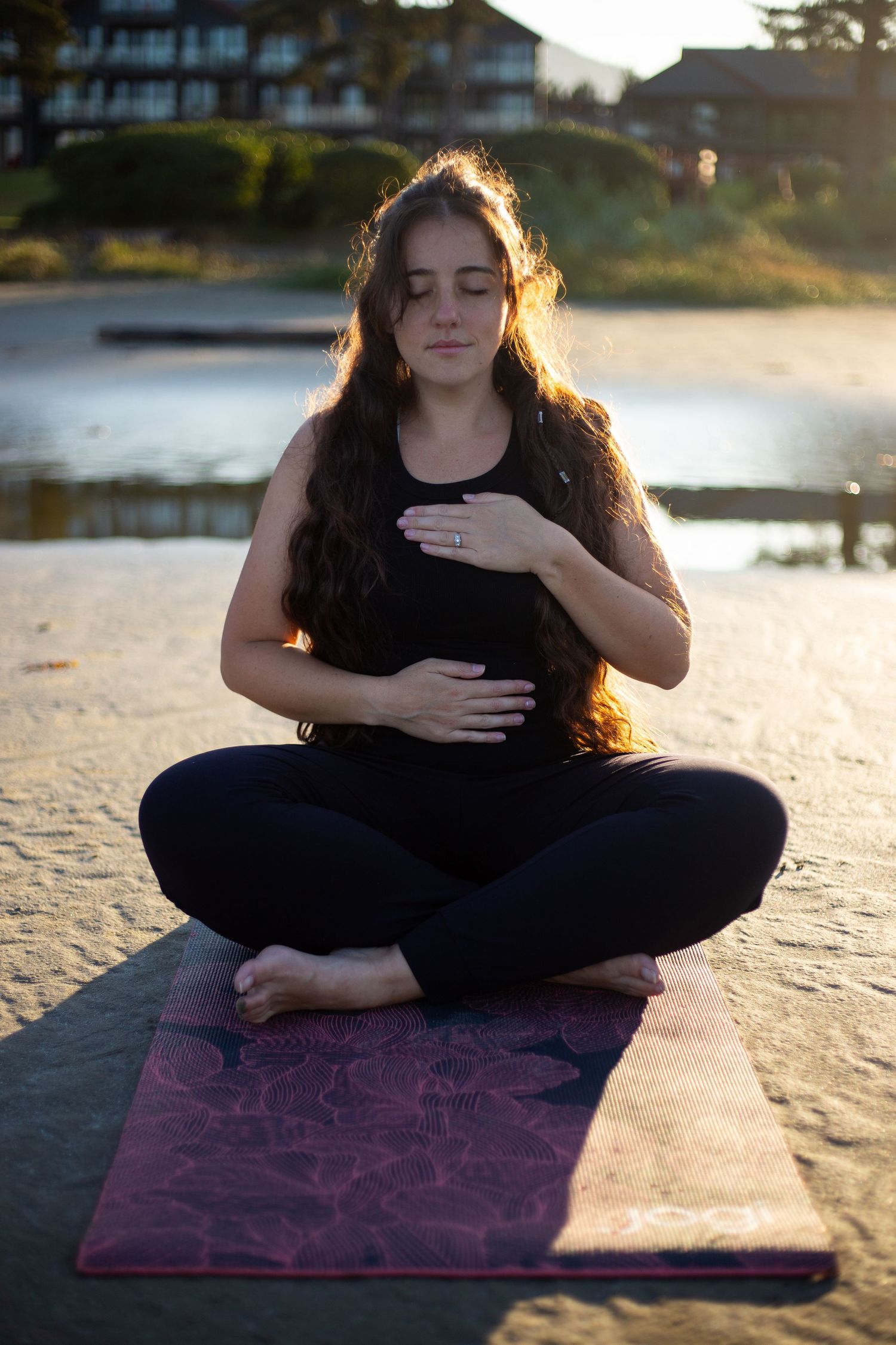 Person practicing mindful meditation on a purple yoga mat at sunset by the water.