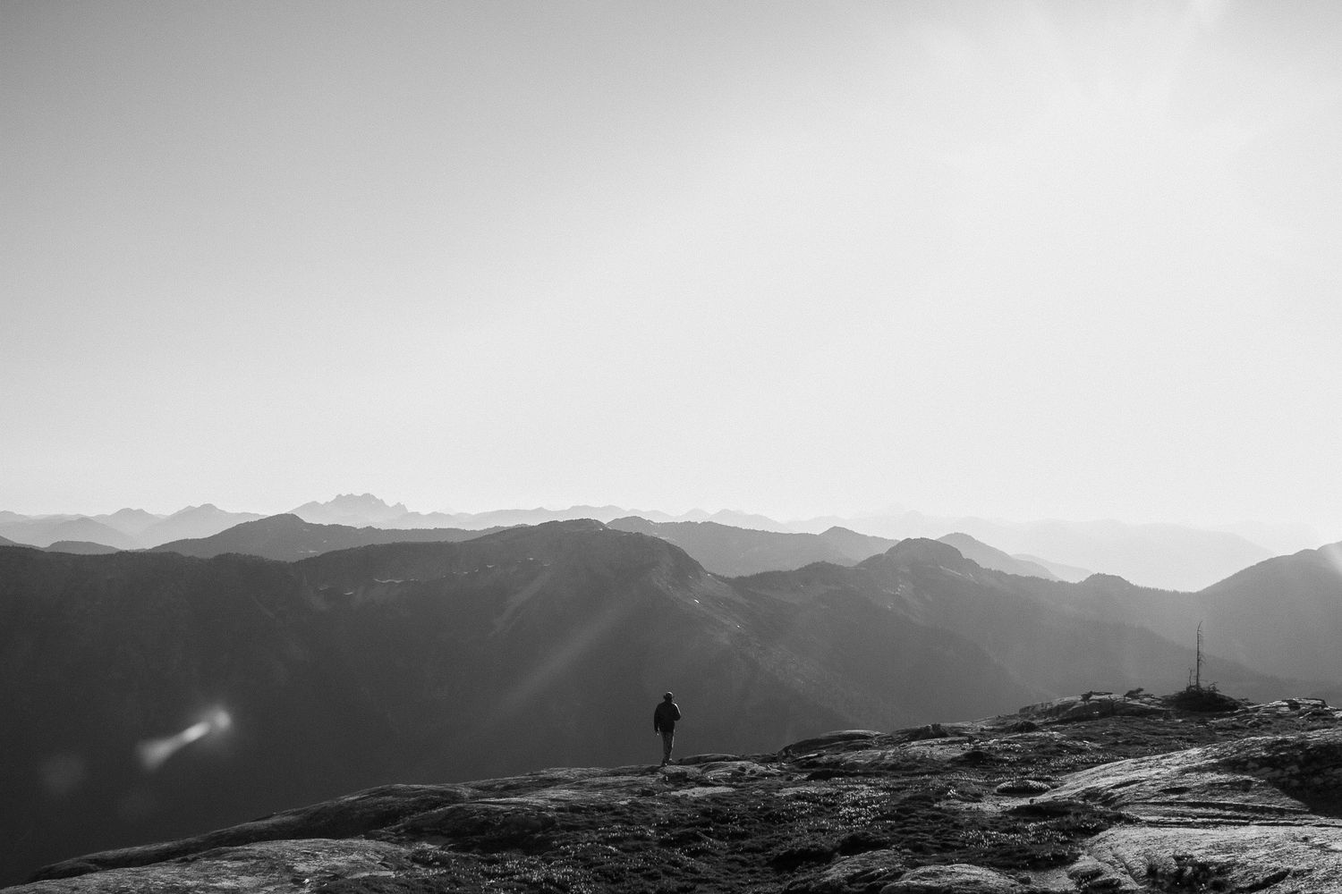 A solitary figure stands silhouetted against a panoramic mountain vista at sunset.