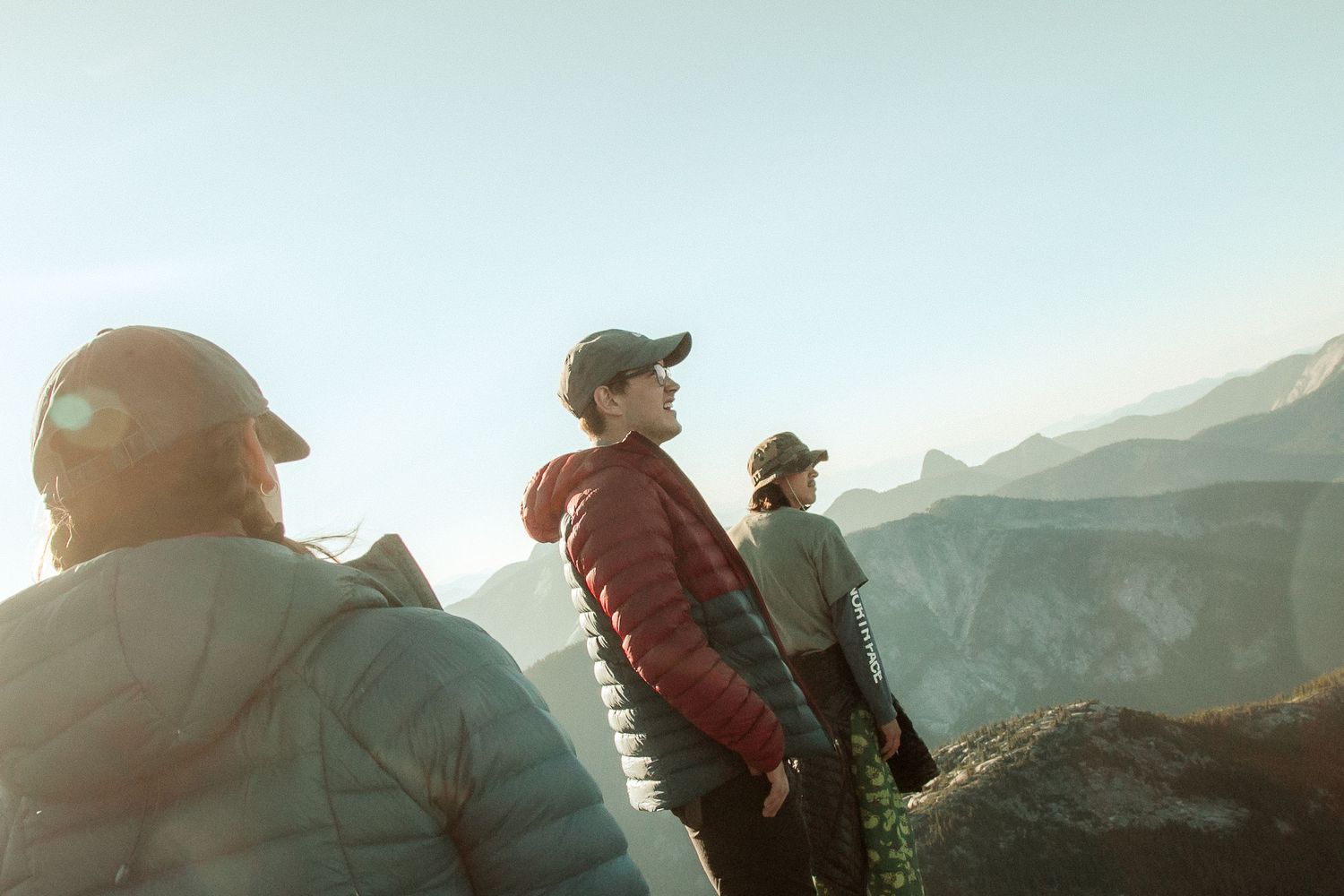 Group of hikers stand on mountain ridge overlooking scenic valley at sunset.