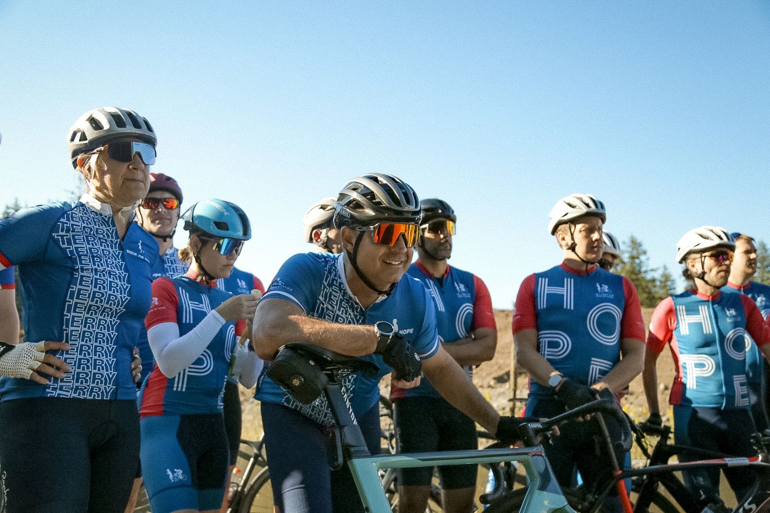 Group of cyclists in matching blue jerseys gathered together during a cycling event.
