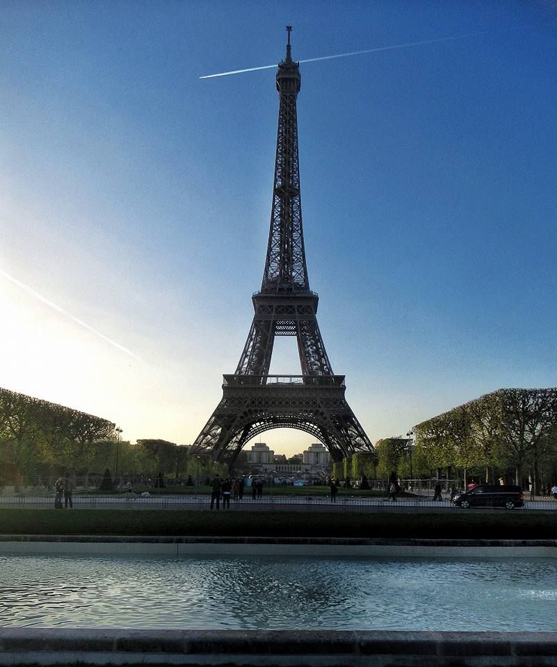 Iconic Eiffel Tower silhouette at sunset with reflections in a pool of water.