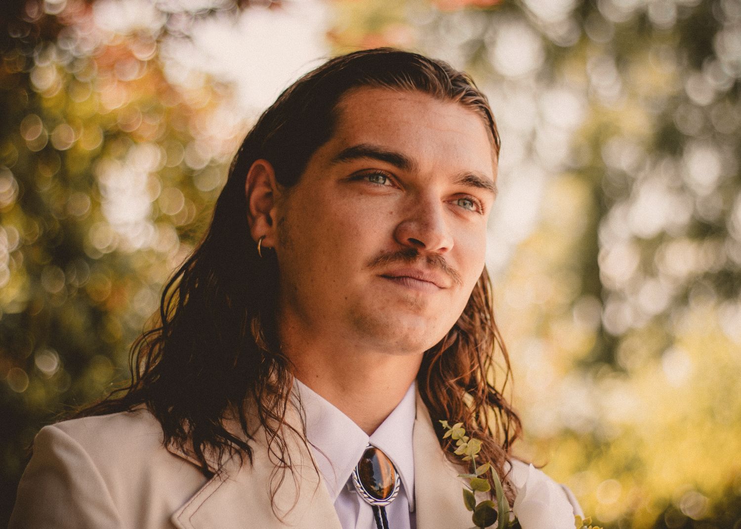 Side profile portrait of person with long hair wearing a white shirt and purple tie outdoors.