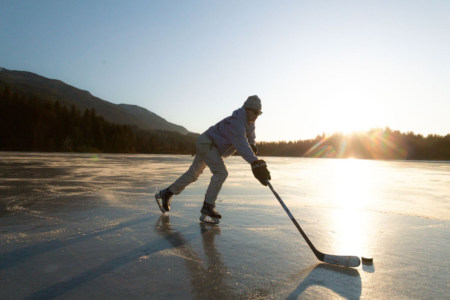 Ice hockey player skating on a frozen lake at sunset with mountains in the background.